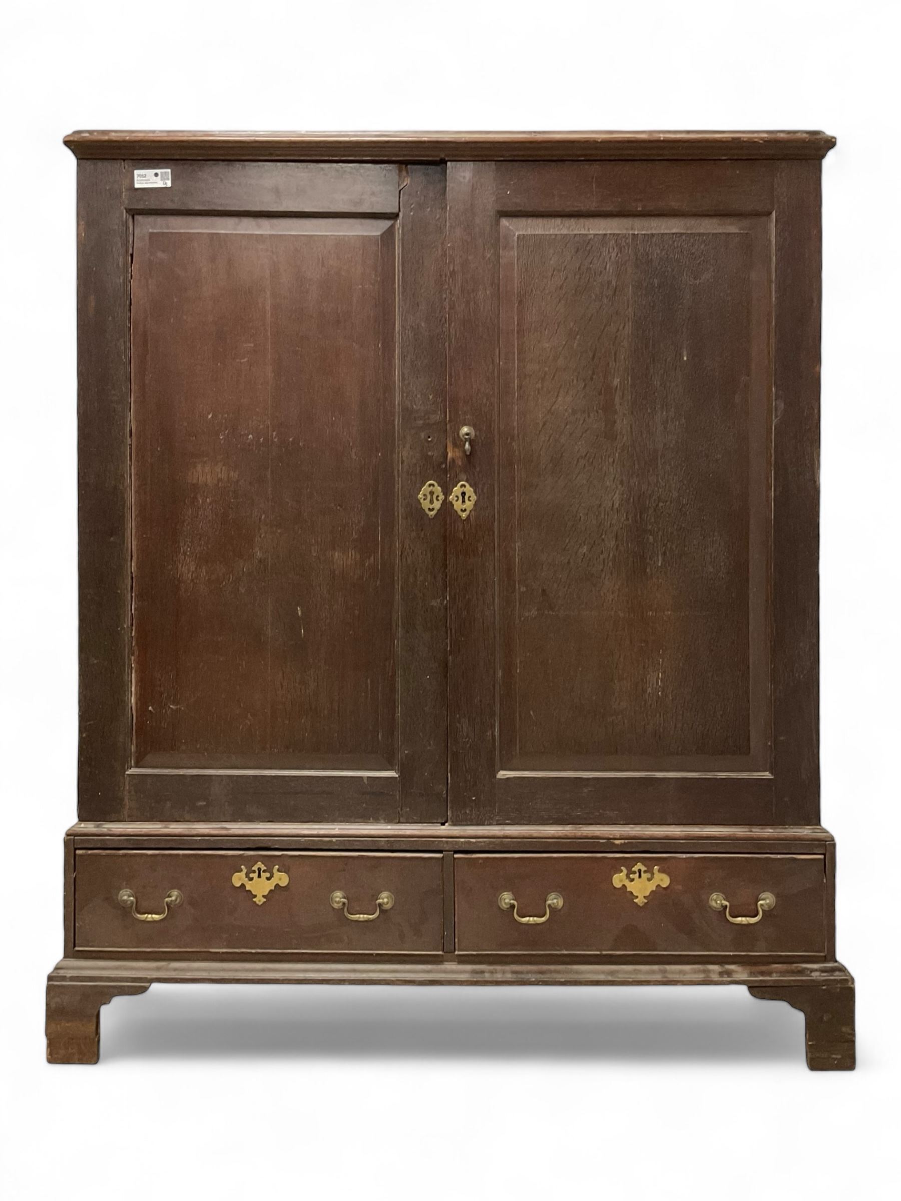 18th century oak linen press, moulded cornice over two panelled cupboard doors, the base fitted with two cock-beaded drawers with pieced brass escutcheons and handles, lower moulded edge on bracket feet