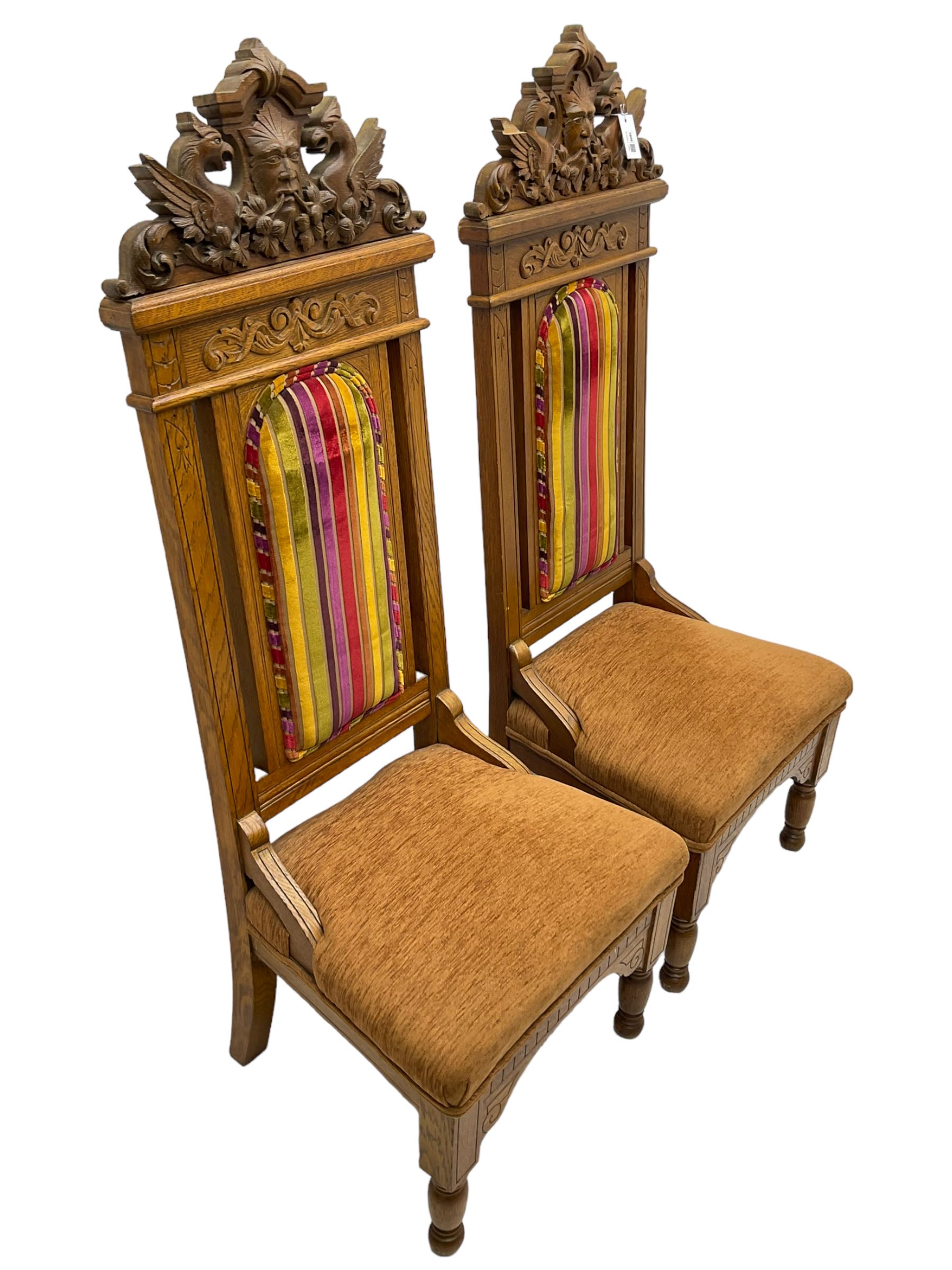 Set of six 20th century Carolean design oak high back chairs, the pediment carved with dragons and central Green Man mask with trailing foliage, the backs upholstered in striped fabric, on turned front supports