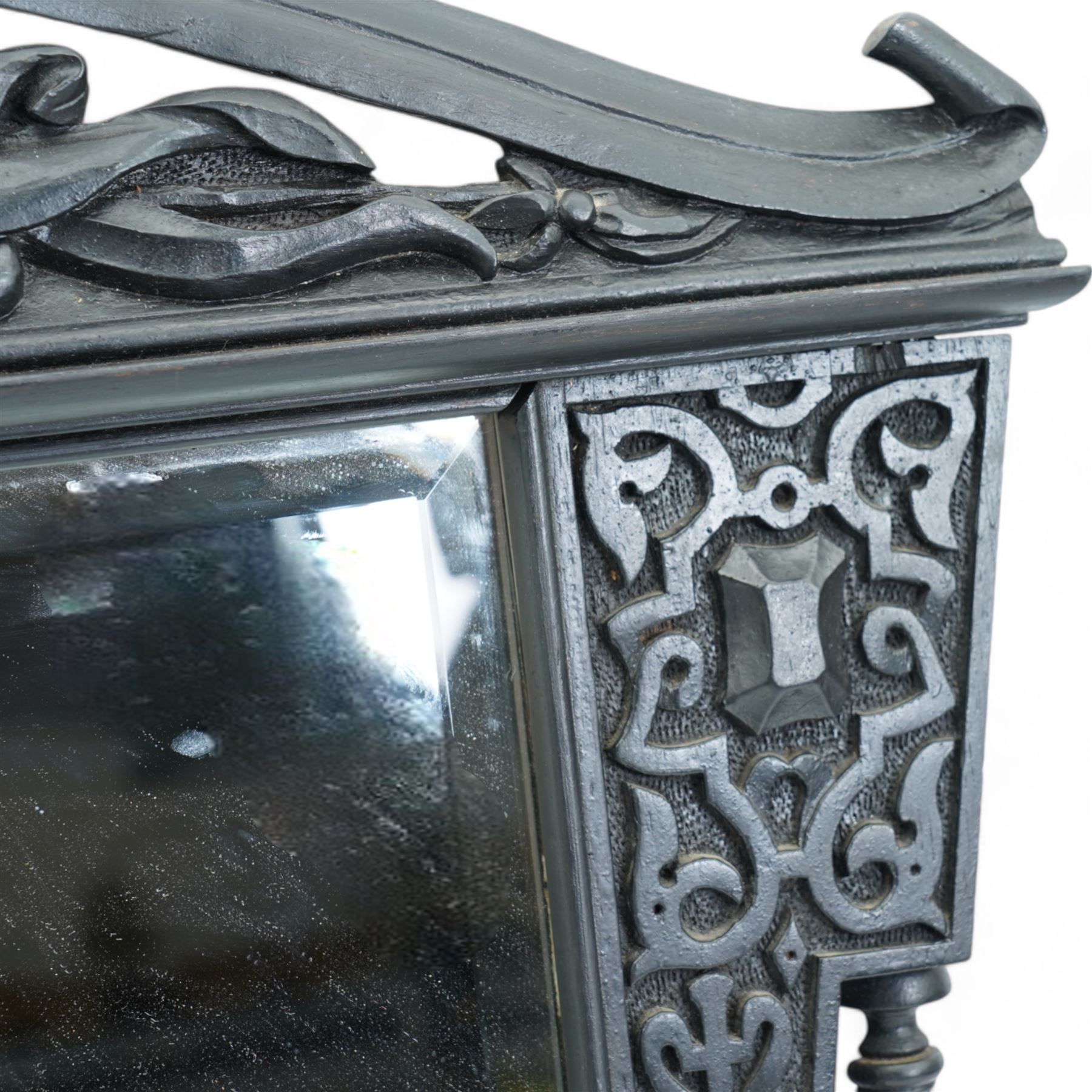 Late Victorian black painted mahogany wall mirror, scrolled pediment with central cartouche inscribed 'E.D', carved strapwork brackets and lower rail with turned supports, bevelled mirror plate 