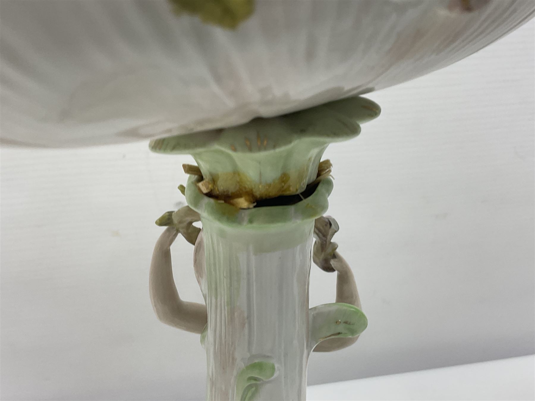 Early 20th century porcelain garniture, the central shaped basket upon a column supported by a female figure, and base with scroll feet, flanked by a pair of four branch candelabra, the scrolling branches and central stem leading to urn shaped sockets over foliate drip pans, upon shaped columns and bases with applied putto, the whole with encrusted flowers throughout, basket H33.5cm, candelabra H52cm