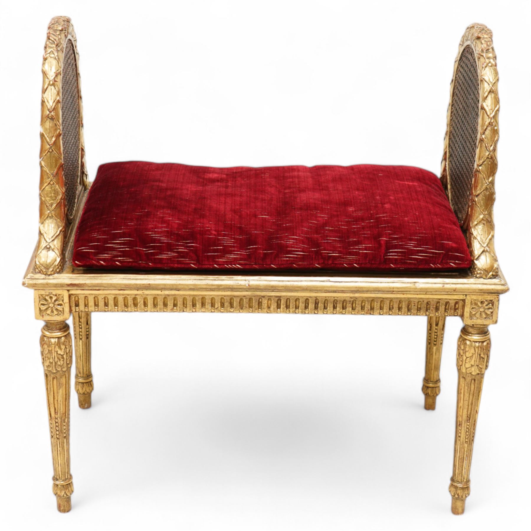 Late 19th century gilt wood and gesso window seat, raised oval cane work sides with lattice and ribbon decorated frame, rectangular cane work seat with upholstered squab cushion, moulded edge over fluted seat rails, on acanthus carved and stop-fluted turned supports 