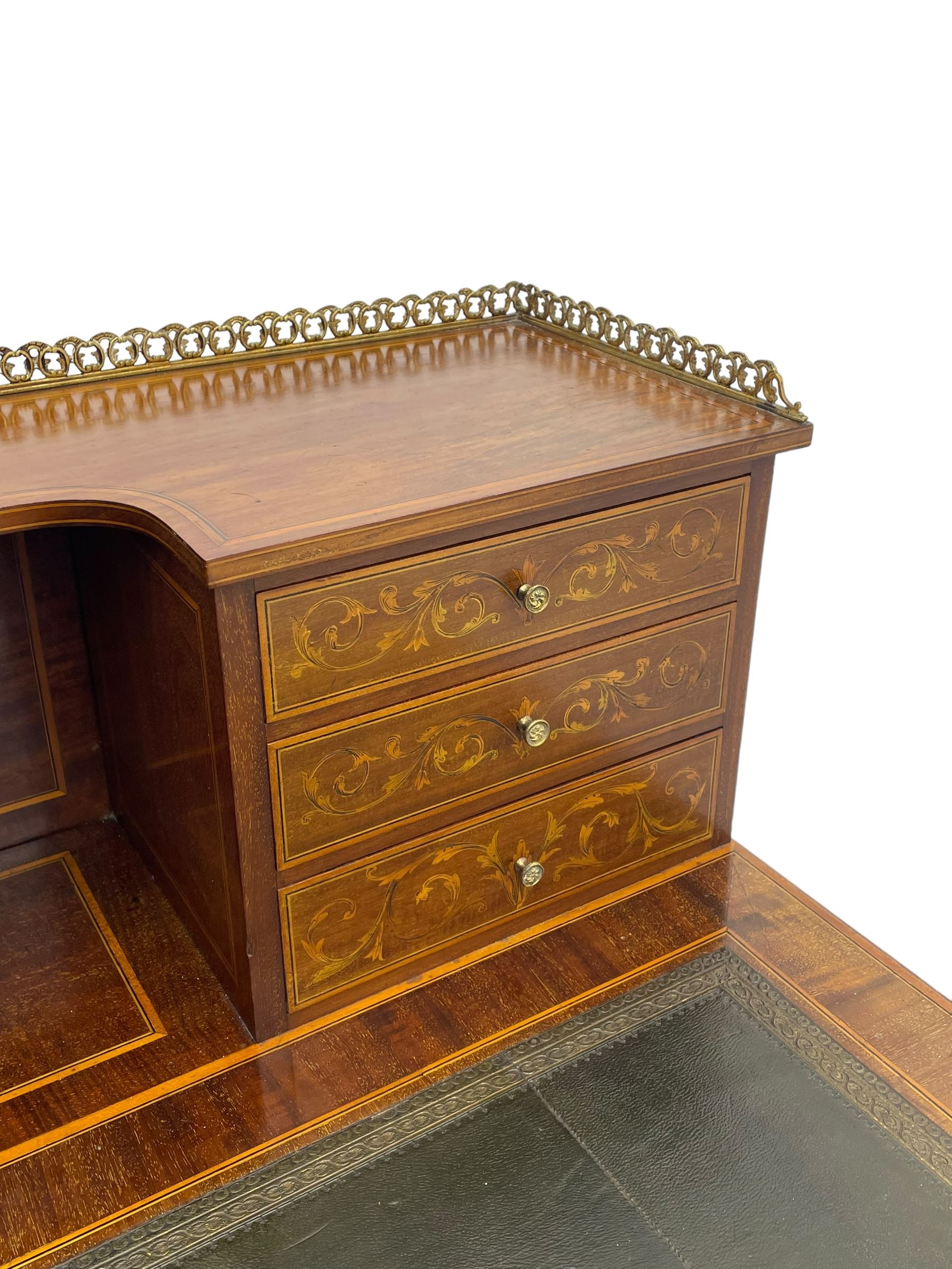 Edwardian inlaid mahogany writing desk, raised galleried back over inlaid central urn with scrolling leafy branches and six small drawers, satinwood banded rectangular moulded top with tooled leather inset, fitted with five drawers, the drawer facias inlaid with scrolling foliage and satinwood banding, square tapering supports inlaid with trailing bell flowers, on brass and ceramic castors 