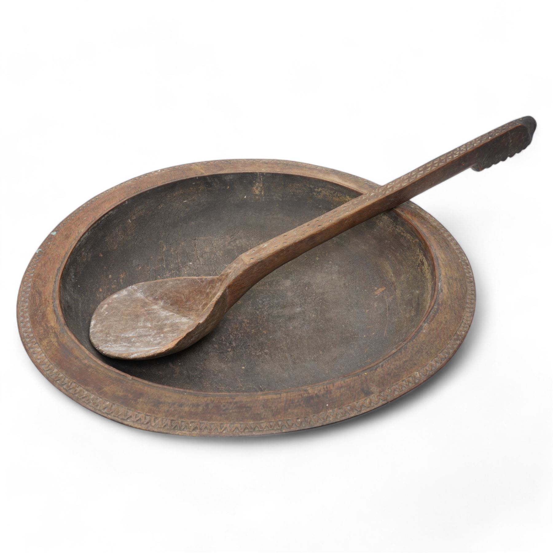 Large African hardwood bowl, of circular shallow form, the rim with chip-carved zigzag decoration, the underneath carved with handles; together with ladle, with similar chip carved decoration D51cm 