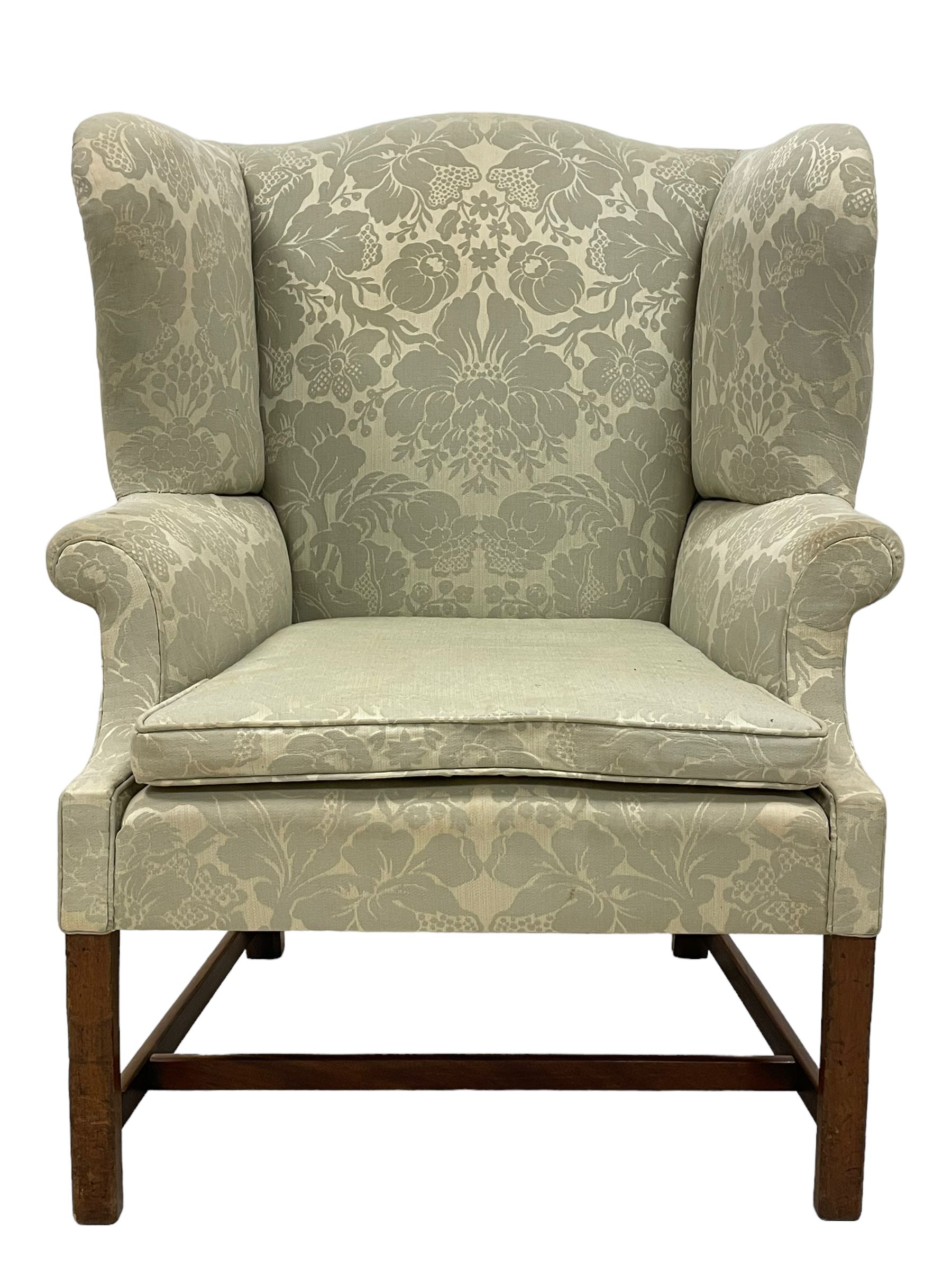 Georgian mahogany framed wingback armchair, upholstered in floral pattern silk damask fabric, wide seat enclosed by rolled arms, on chamfered square supports united by plain stretchers 