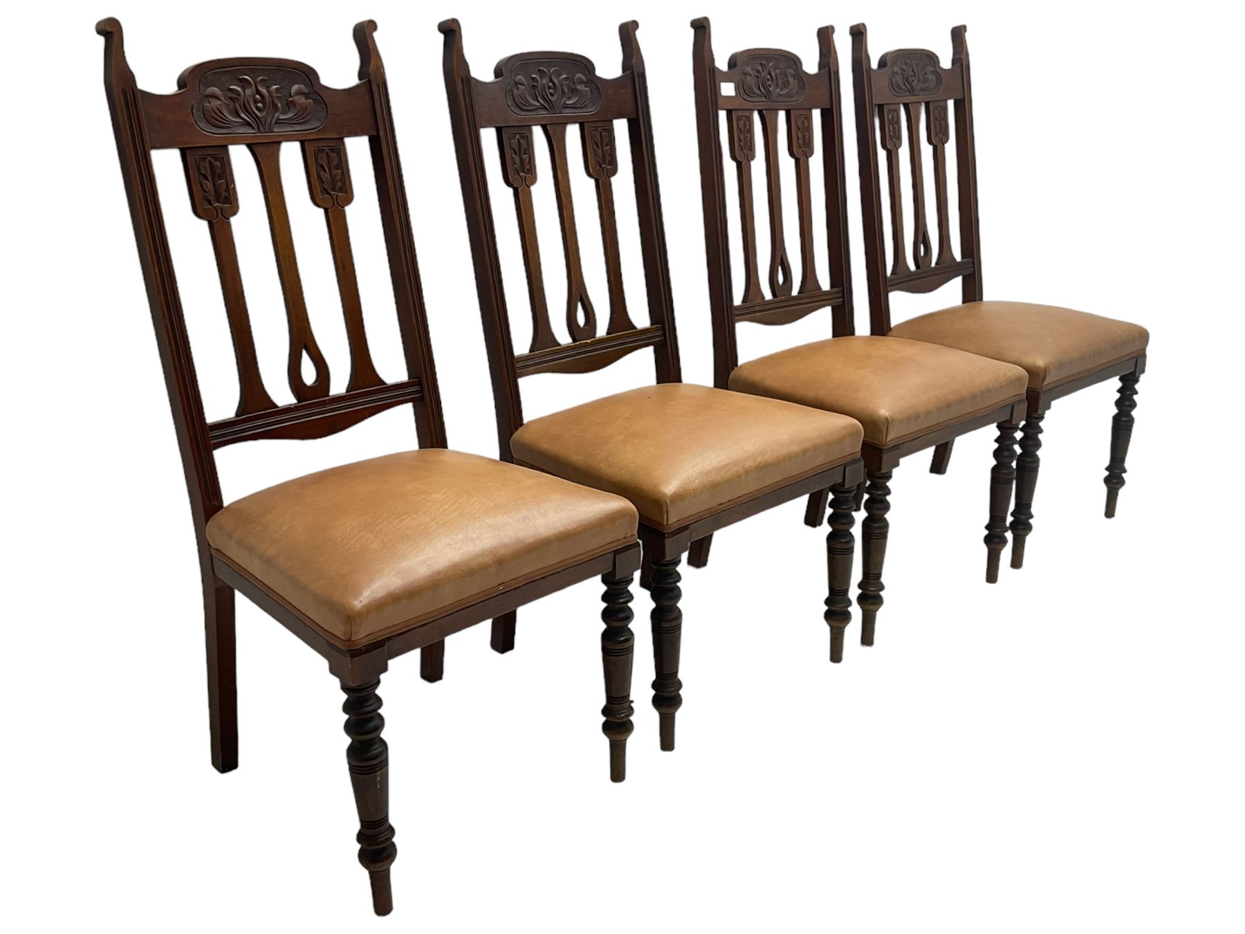 Set of four Edwardian walnut dining chairs, foliate carved high back over sprung seat upholstered in tan faux leather, raised on turned supports