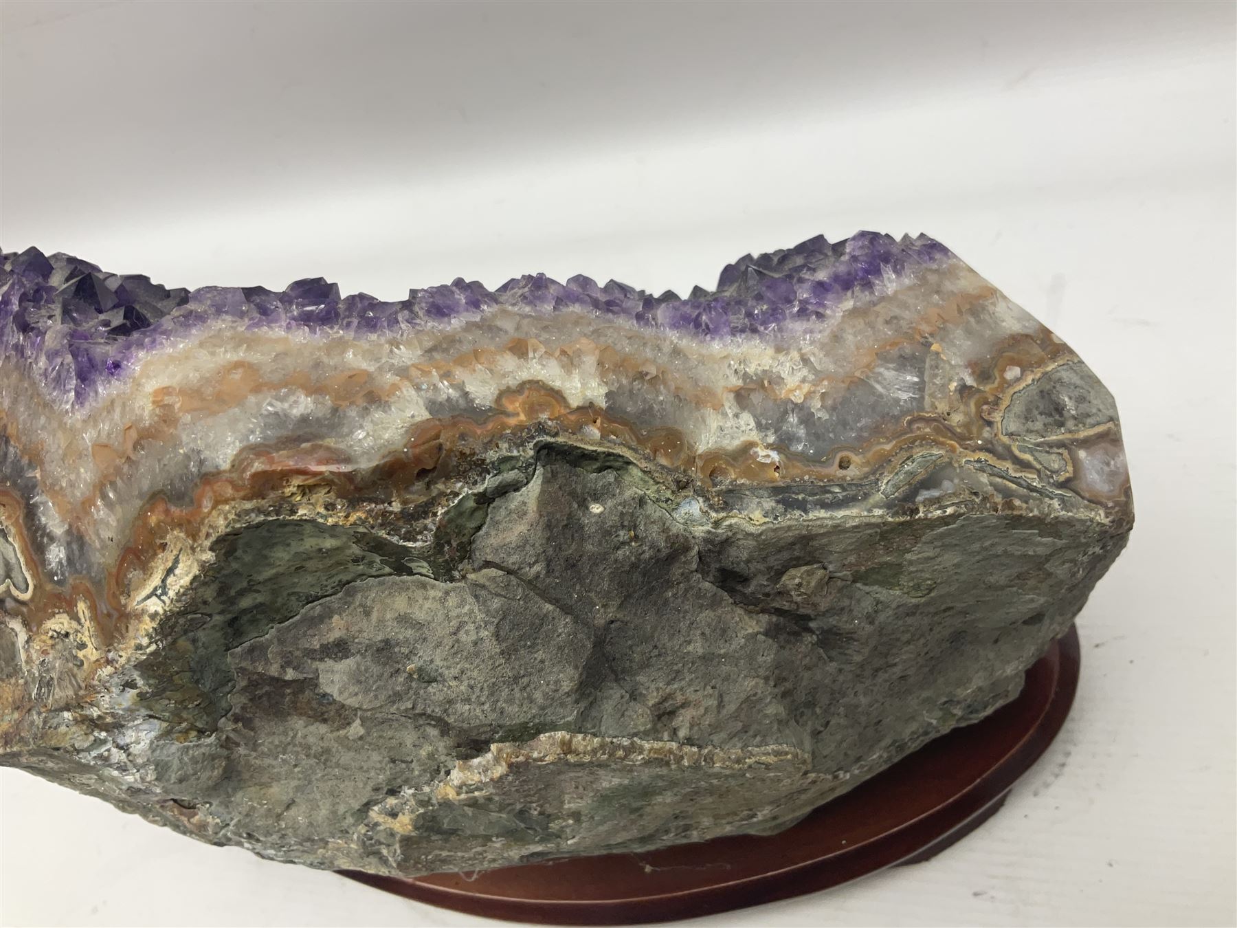 large amethyst crystal geode cluster, with well-defined crystals of various sizes, upon a carved wooden stand 