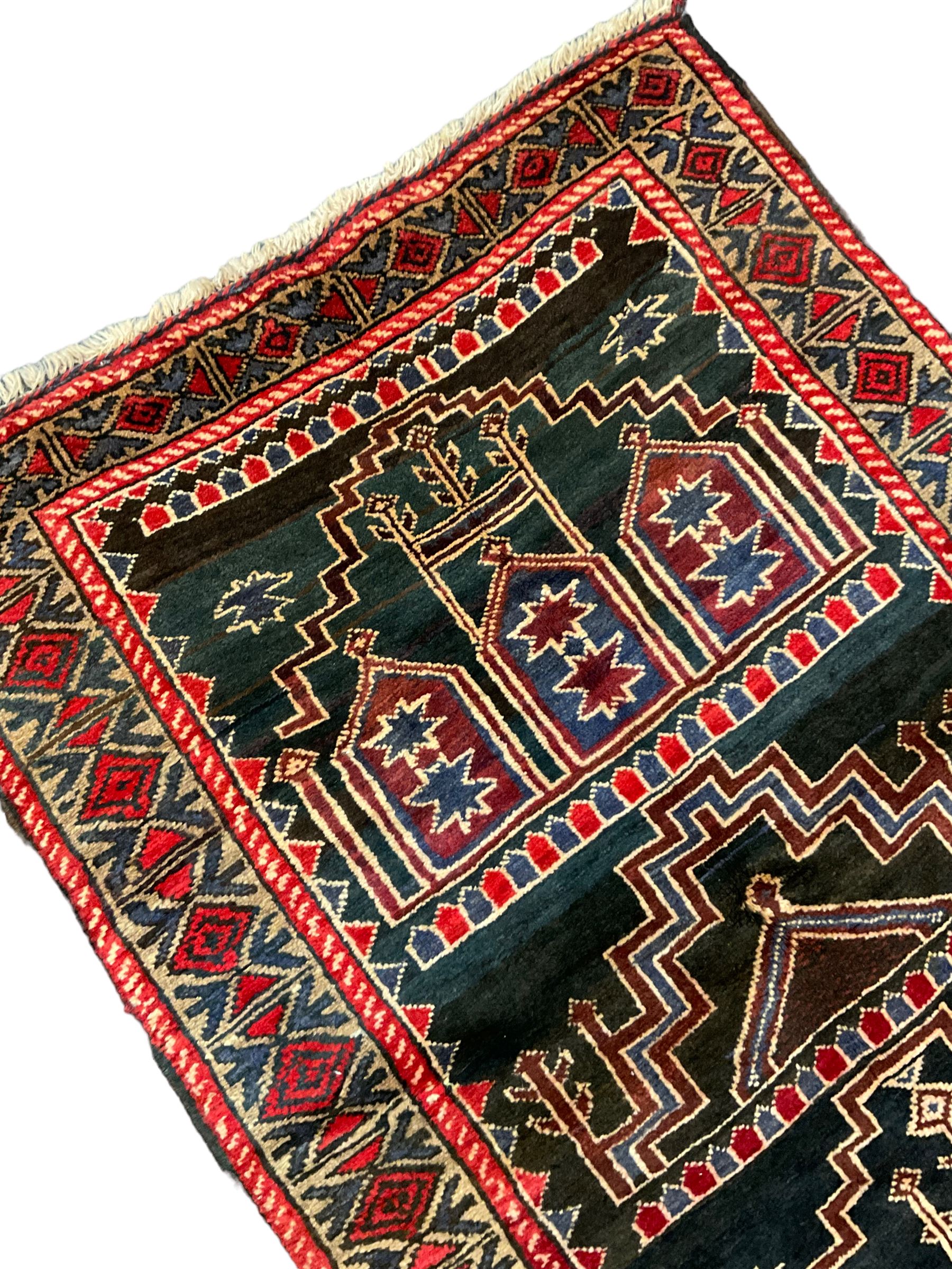 Baluchi dark indigo and crimson ground rug, decorated with cityscape within geometric border 