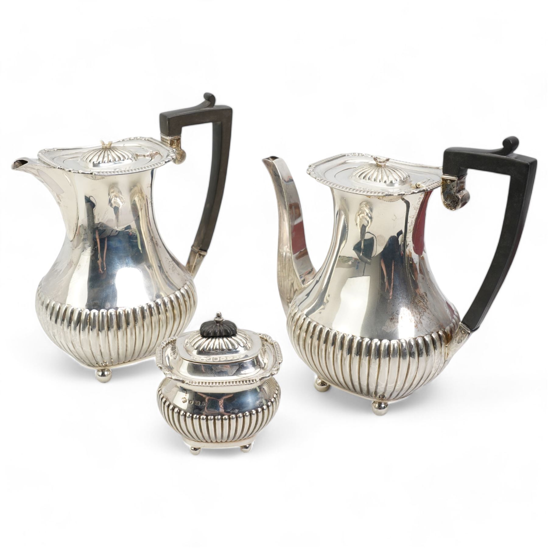 Silver three piece coffee set comprising coffee pot, hot water jug and sugar box each with half body fluted decoration, gadrooned edge, ebonised handles and ball feet, Sheffield 1927 Maker William Hutton & Son Ltd