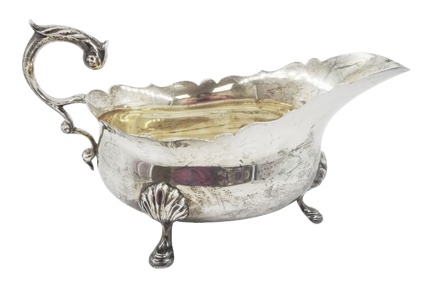 1930s silver sauce boat, of typical form with shaped rim, and acanthus leaf capped flying scroll handle, upon three palmette mounted stepped feet, hallmarked 	Harrods Ltd, London 1934, including handle H10.4cm