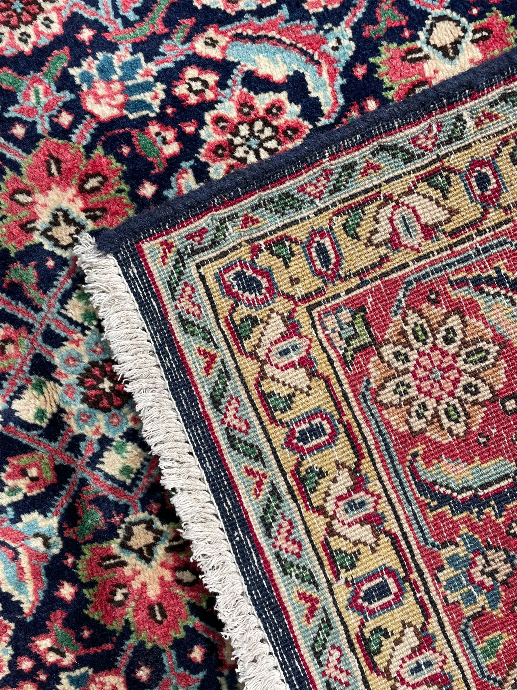 Persian Farahan indigo ground rug, the field decorated with large repeating floral herati motifs, crimson ground border decorated with palmettes and trailing leafy branch, within guard stripes 