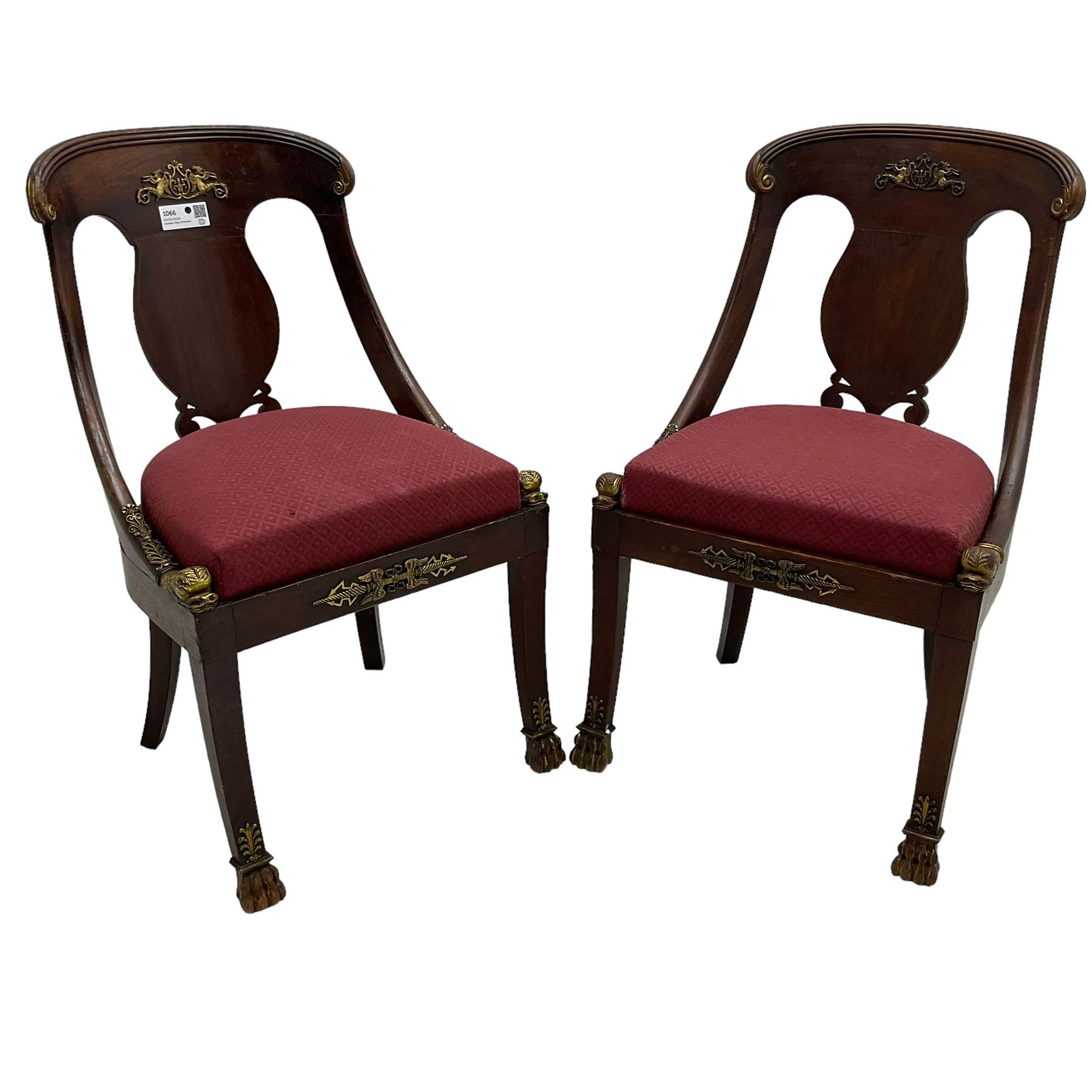 Pair of French Empire mahogany spoon0back side chairs, reeded cresting rail with scrolled ends over a shaped and pierced back splat, decorated with gilt metal mount in the form of winged classical maidens playing panpipes, drop-in seat upholstered in crimson lozenge patterned fabric flanked by gilt stylised scaled fish mounts, the apron with neoclassical gilt metal mounts, raised on sabre supports with paw feet