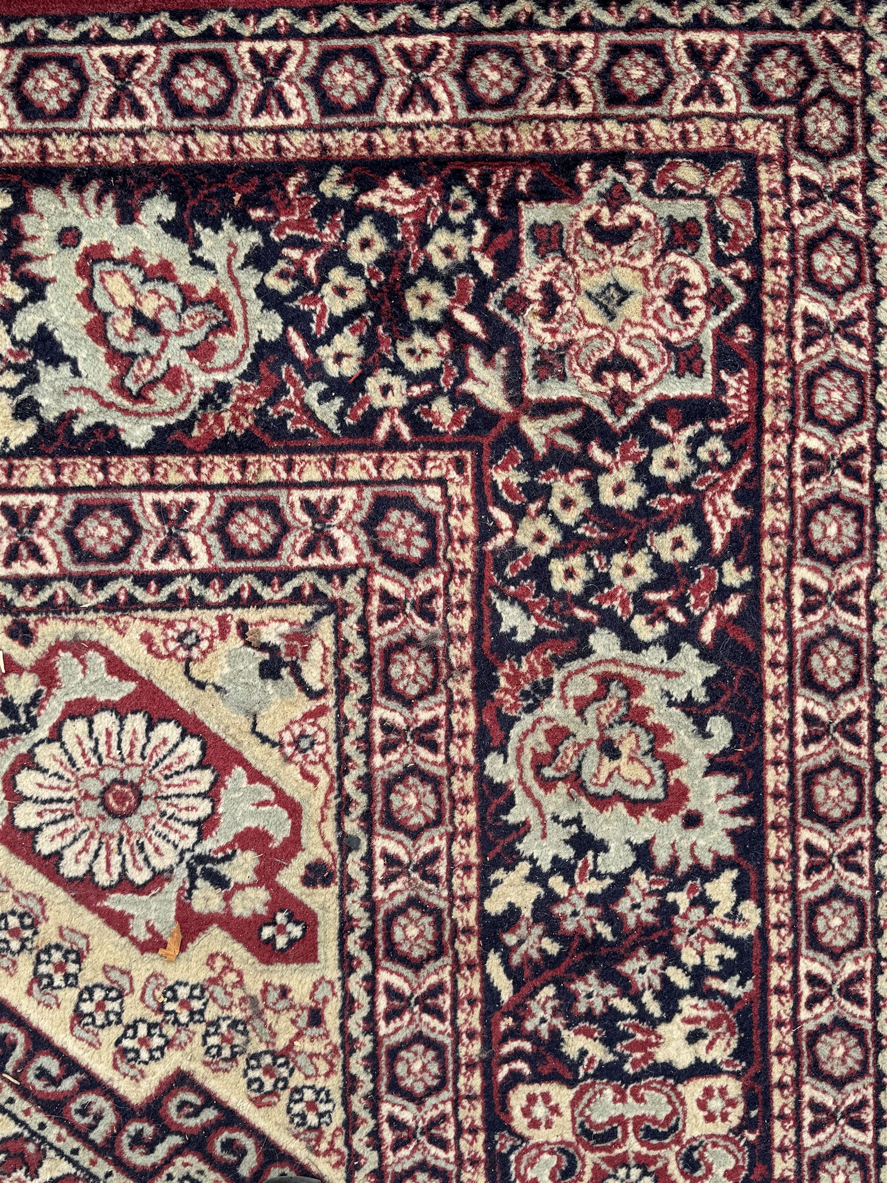 Persian Heriz design red ground carpet, the field decorated with a central star-shaped medallion surrounded by geometric floral motifs and angular vine patterns, the spandrels highlighted with palmette designs, the main border featuring a series of stylised rosettes and leaves against a dark blue ground, enclosed by multiple guard stripes with alternating floral and geometric motifs