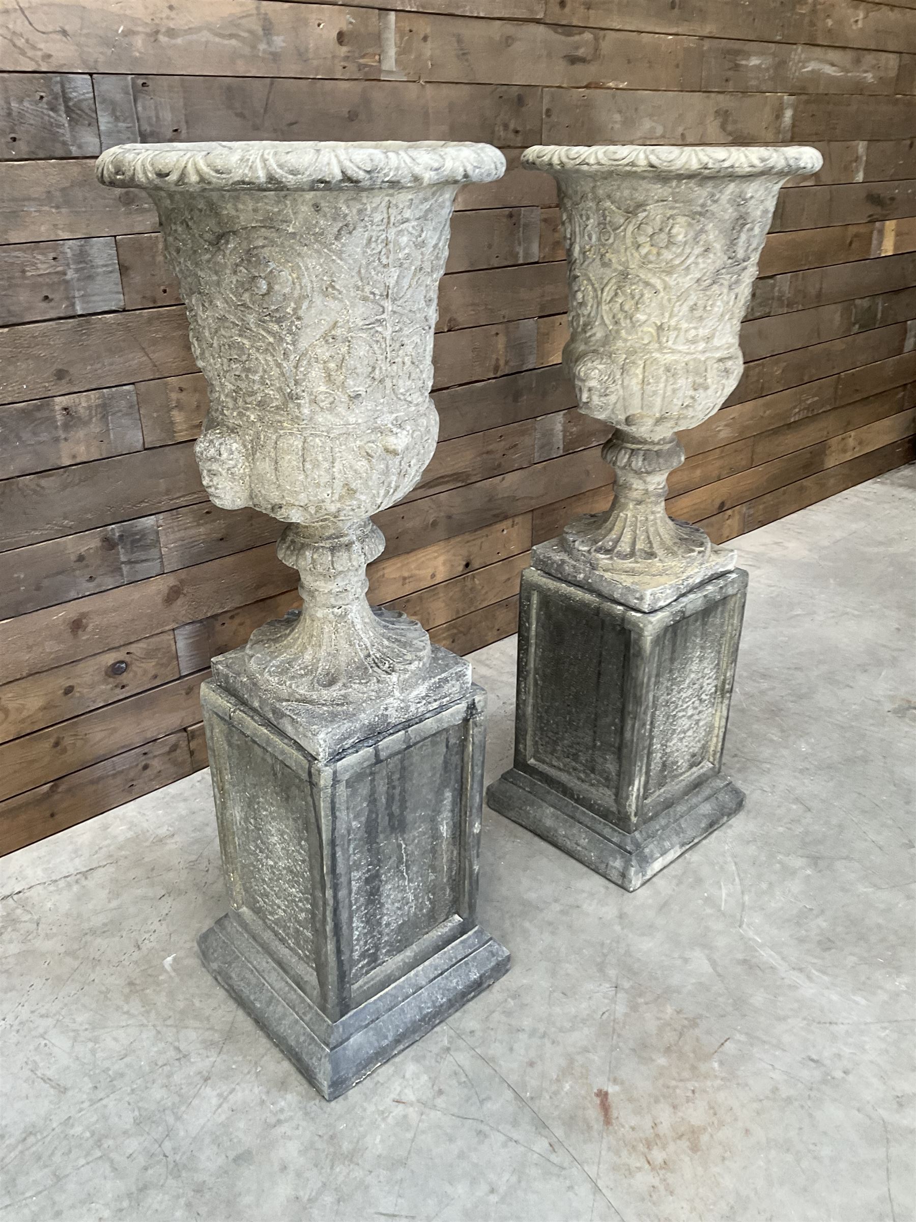 Pair of Georgian design cast stone garden urns, egg and dart rim with raised floral motifs, pedestal base terminating on square plinth, raised on square block plinth