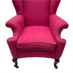 Georgian design hardwood-framed wingback armchair, arched cresting rail over curved wingback, rolled arms on scrolled cushioned supports, reverse bow-front, upholstered in claret red fabric with loose seat cushion, on cabriole front feet and brass castors 