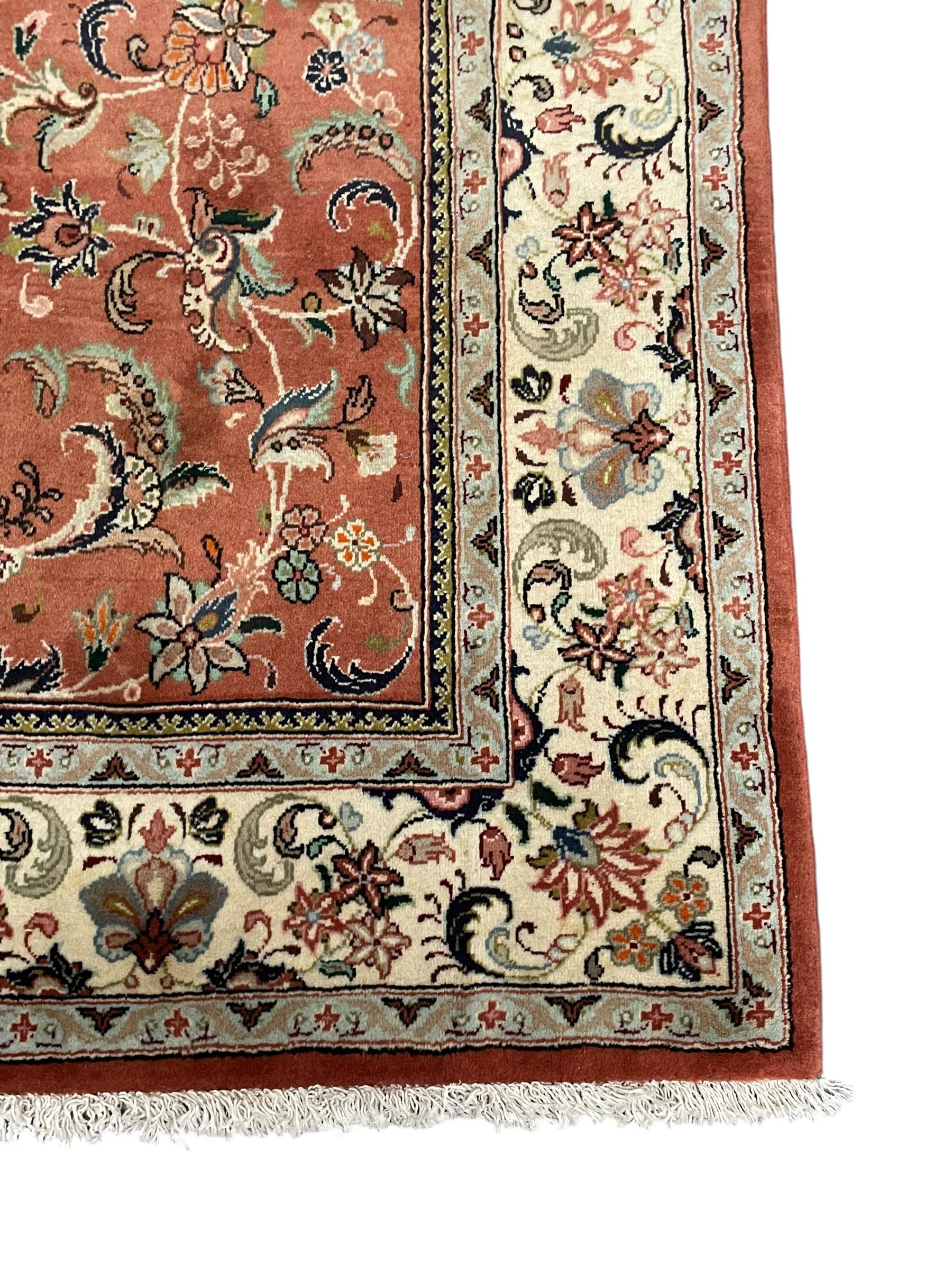 Persian Kashan peach ground rug, the field decorated with swirling leafy branches and stylised plant motifs, ivory ground border with trailing foliate design interspersed with flower heads, within guard stripes 