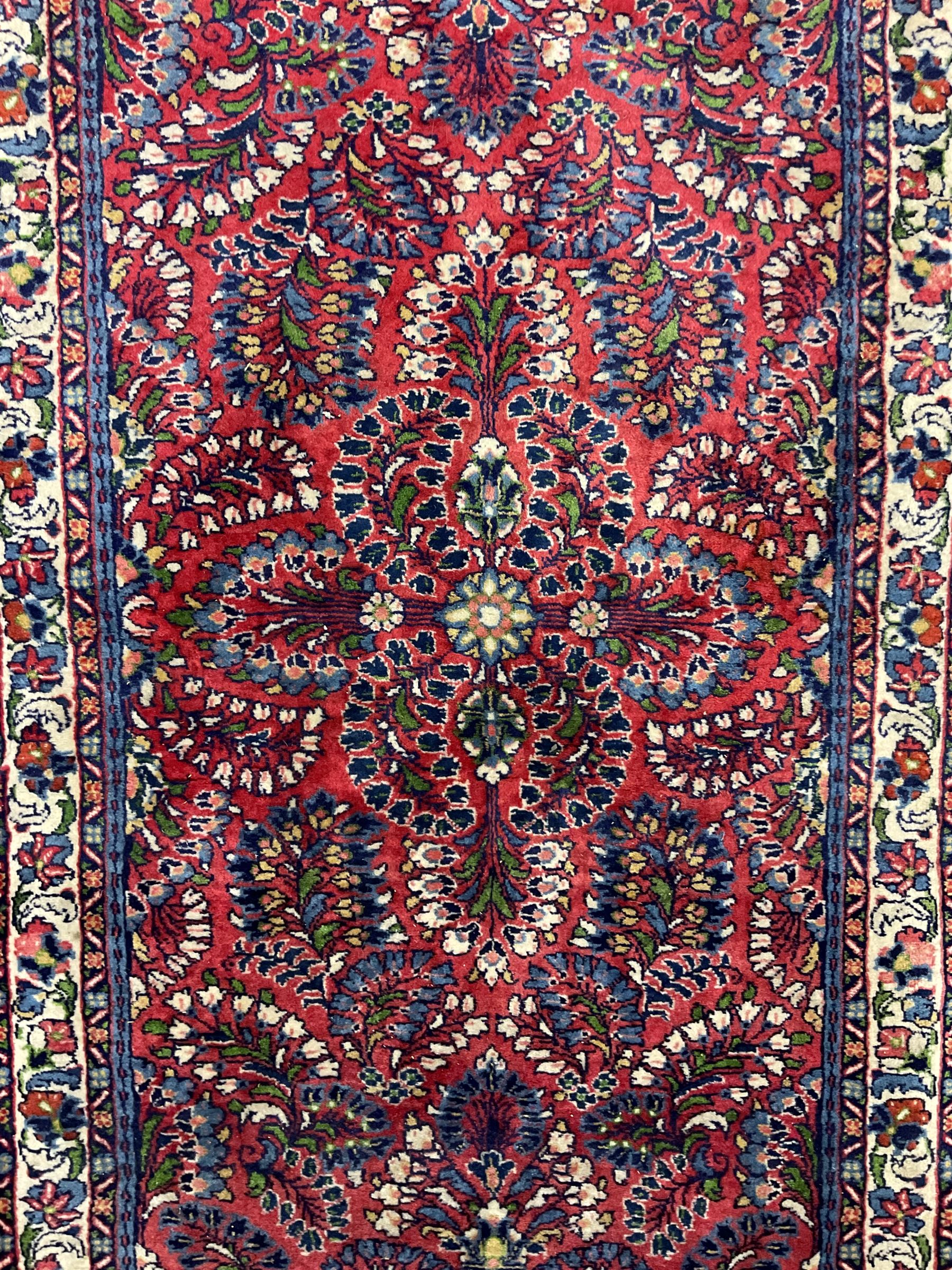 Small Persian red ground rug, the field decorated with an overall floral design, guarded ivory ground border decorated with trailing flower heads and foliage