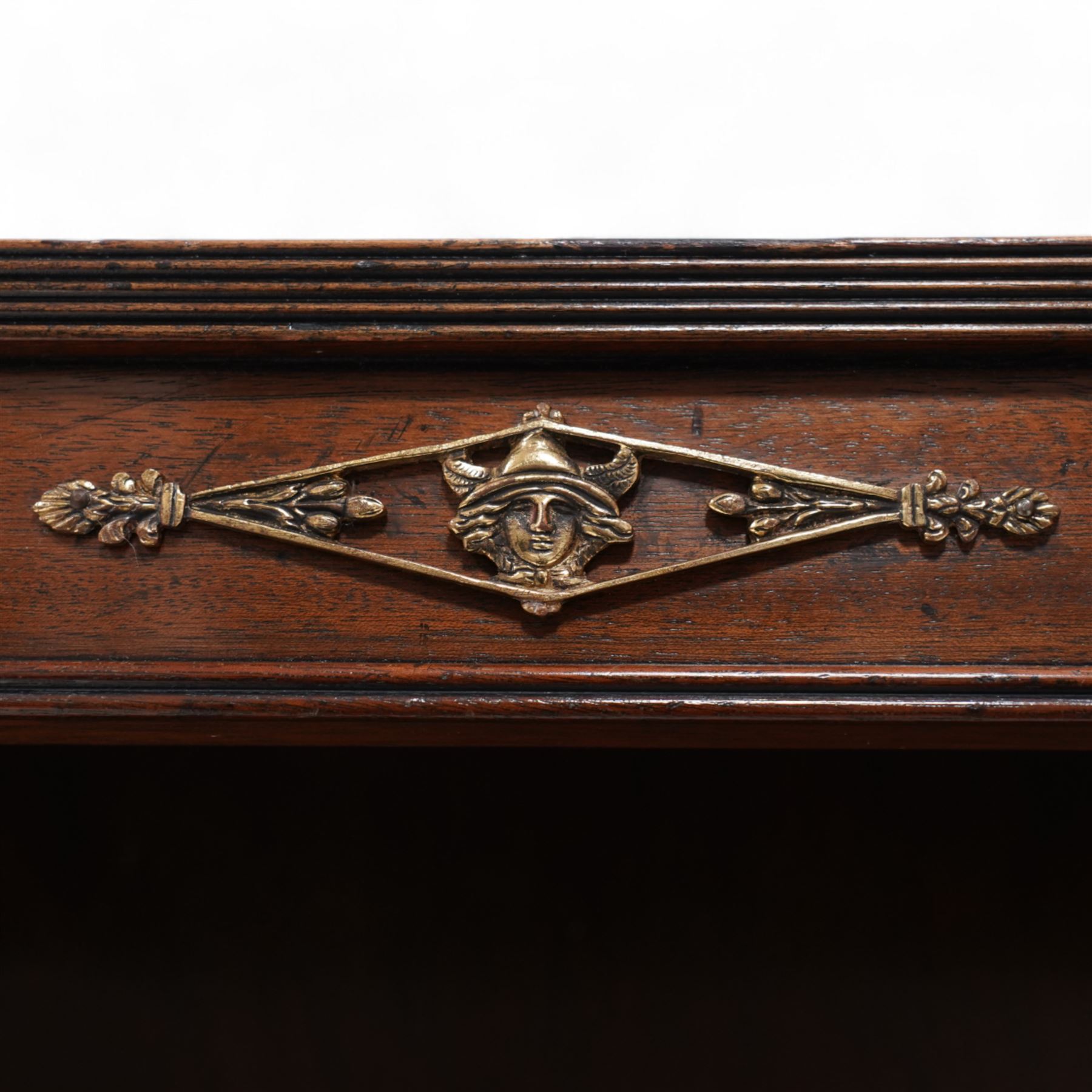 Pair of Neoclassical Empire design mahogany open bookcases, the rectangular top with reeded edge over a plain frieze decorated with a brass mount of the Greek god Hermes, the single shelf flanked by reeded square pilaster uprights, surmounted by a brass capital in the form of a female Egyptian bust, with human feet terminals, lower moulded edge on skirted base