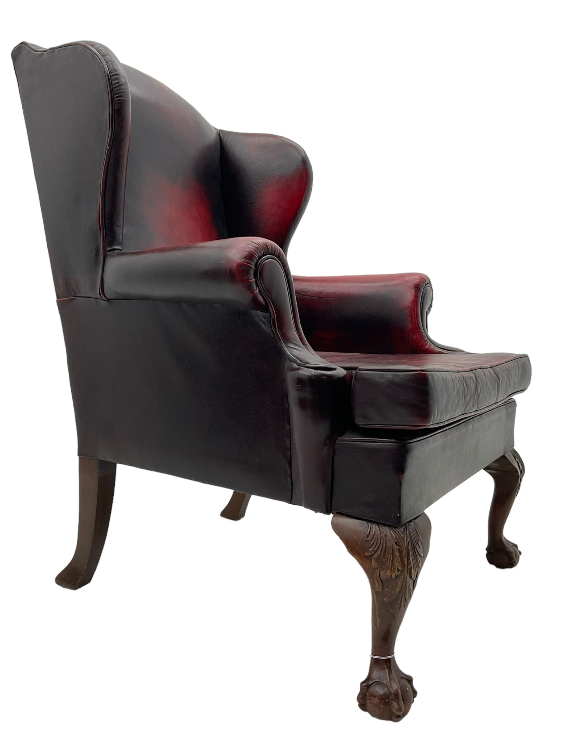 Georgian design hardwood-framed wingback armchair, upholstered in red leather, loose seat cushion and rolled arms, on acanthus carved ball and claw front feet 