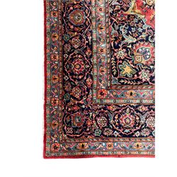 Persian Kashan crimson ground carpet, central rosette medallion on a field of trailing foliate branches decorated with palmettes, scrolling border with repeating plant motifs and flower heads, enclosed within floral pattern guard stripes