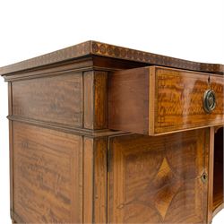 Waring & Gillow - Edwardian Sheraton Revival satinwood sideboard, shaped and stepped break bow-front, the top with central oval book-matched veneered panel and rosewood banding, the front and return edges inlaid with a single row of repeating circles, three frieze drawers each inlaid with rosewood band and ebony stringing, two cupboards flanking open centre, the doors inlaid with lozenges and satinwood cross bandings, on faceted octagonal supports with foliate carved collars, terminating to turned feet, the central drawer with 'Warings' metal plaque and stamped 'Gillows'