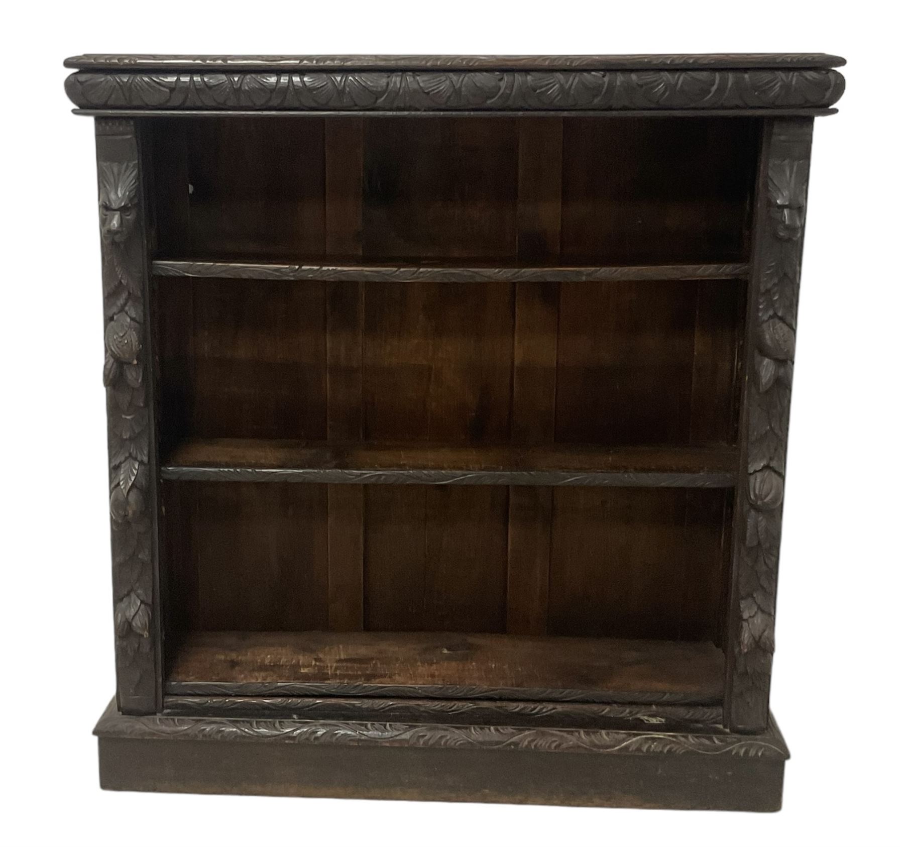 Victorian Jacobean revival carved oak open bookcase, cushion frieze carved with foliate decoration the pilasters decorated with applied carved lion masks and fruit motifs with extending leafage, two shelves over skirted base