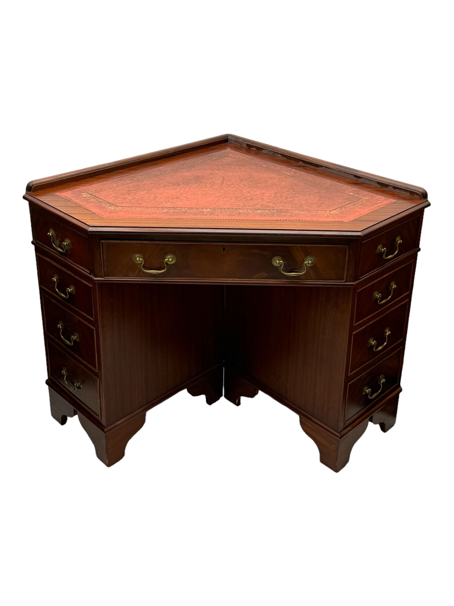 Late 20th century mahogany corner desk, leather inlaid top with gilt tooling, central frieze drawer flanked by two banks of four graduated drawers, raised on shaped bracket supports 