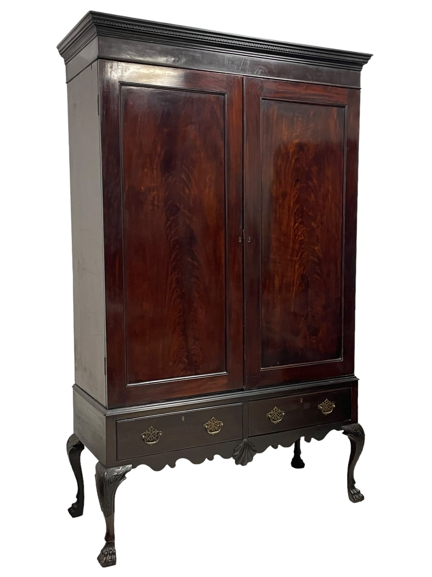 19th century Irish mahogany press wardrobe, projecting dentil cornice over two figured panelled doors, enclosing three sliding trays and hanging rail with coat hooks, fitted with two drawers to base over a shaped apron, raised on acanthus carved cabriole supports with paw feet, retailed by Millar & Beatty of Dublin, with paper labels verso, collected and restored by Michael Butler (1870-1900), impressed stamp to side and ink stamp to drawer inscribed 'M Butler collector of high-class furniture and works of art'