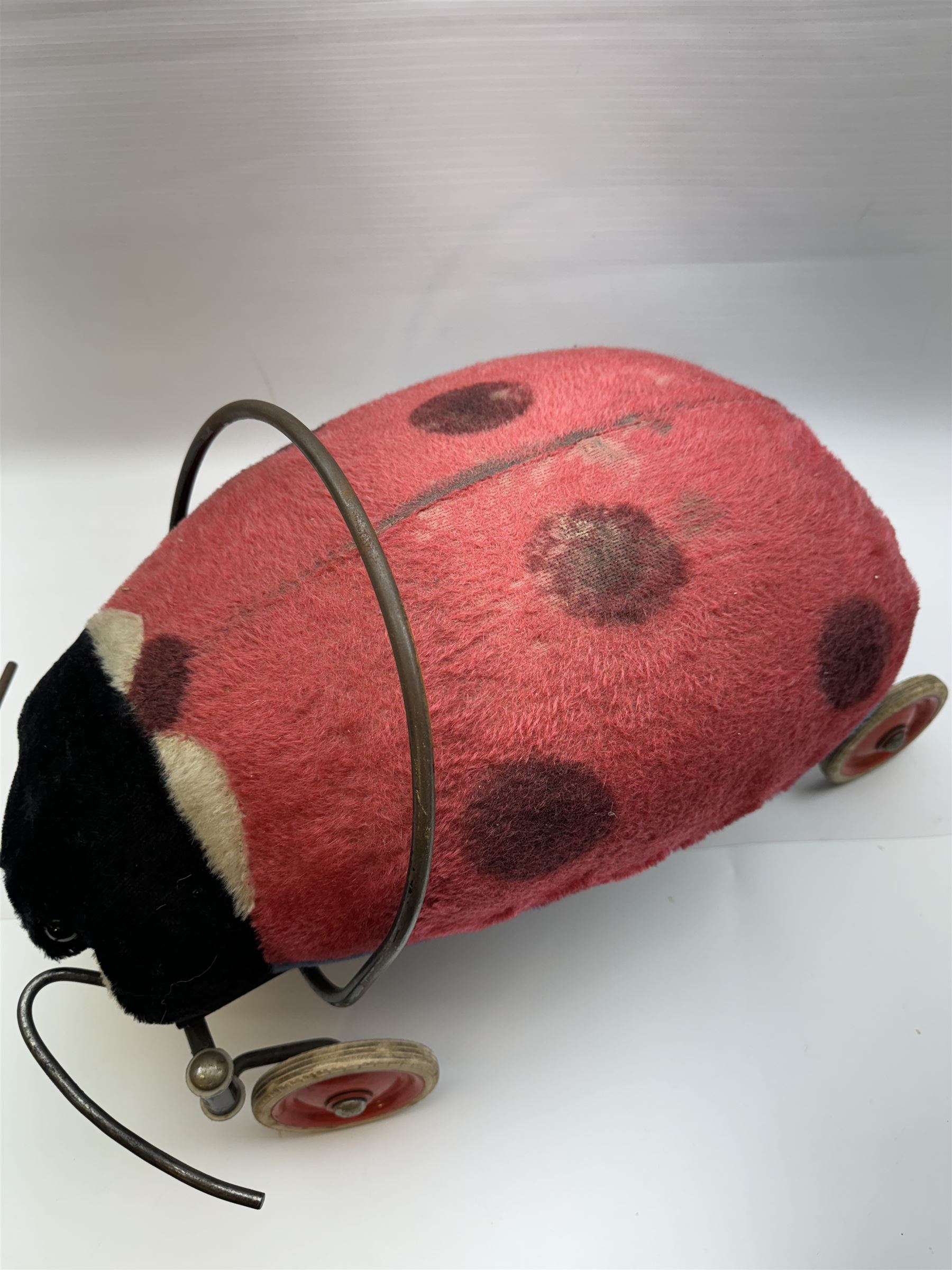 Steiff child's ride on ladybird, circa 1950s, the mohair body with red and black spotted seat, black and white face and blue underbelly, upon a metal frame with rubber and metal wheels, H30cm, W52cm