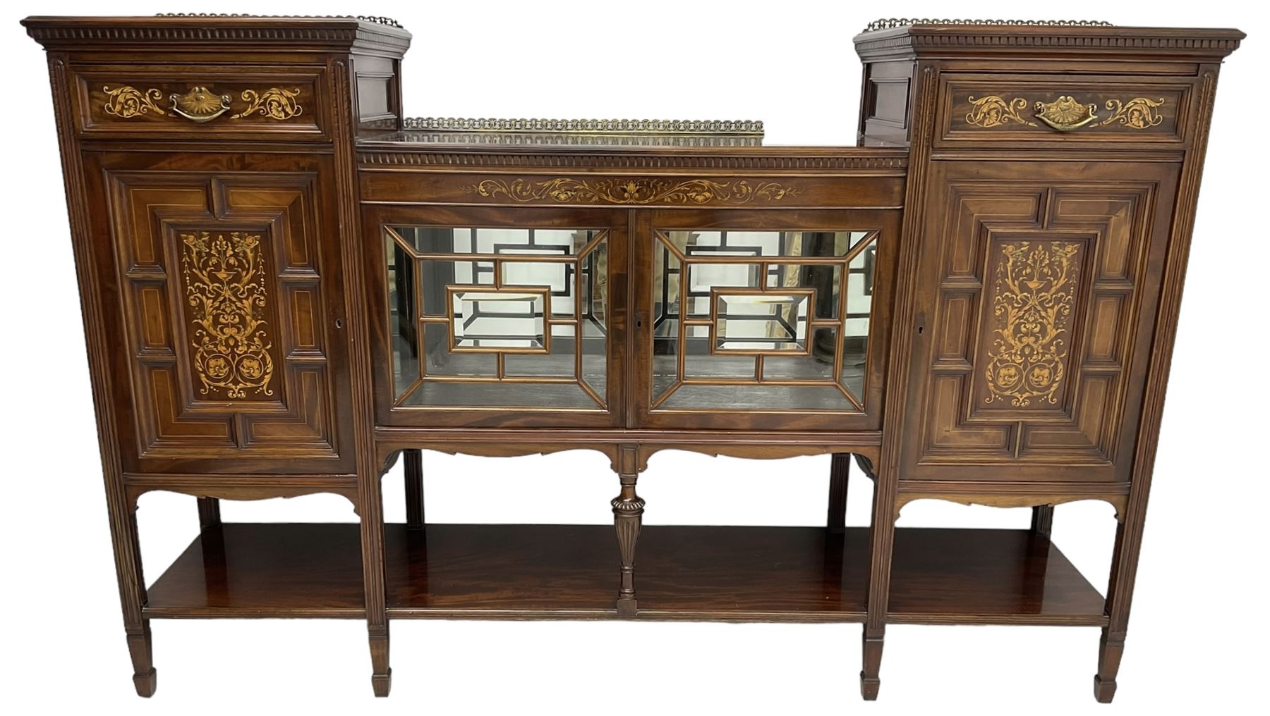 Late Victorian mahogany drop-centre sideboard, moulded and dentil top with raised cast metal galleries, fitted with two drawers and two panelled cupboards, central display cabinet enclosed by two astragal and bevel glass glazed doors, inlaid with curled acanthus leaves and fruit cornucopias, moulded uprights terminating to square tapering spade feet, united by undertier 