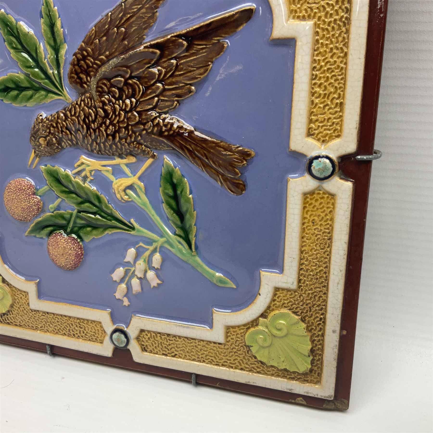 19th century Minton & Co majolica tile, decorated in relief with a bird upon a fruiting branch against a blue ground, with textured ochre border and anthemion to each corner, impressed mark verso, H19.7cm