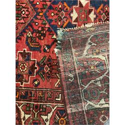 Persian Hamadan rug, red ground with overall geometric design, the field with three extended lozenges, decorated with geometric and stylised flower head motifs, the border and guards decorated with repeating geometric motifs