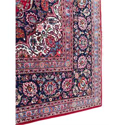 Large Persian Kashan crimson ground carpet, central floral medallion surrounded by swirling leafy branches and palmettes, enclose by floral pattern spandrels, the indigo border with overall scrolling design decorated with palmettes, within guard stripes 