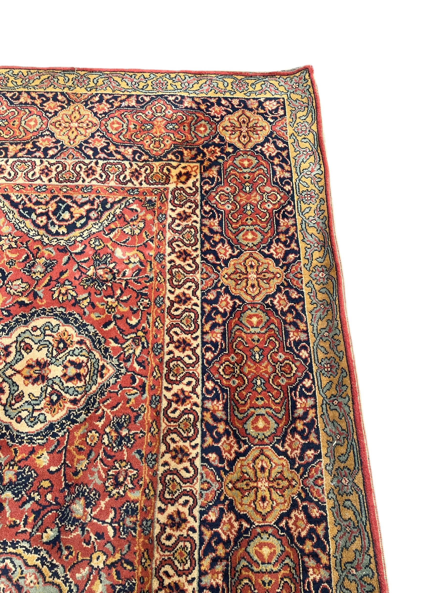 Large Persian design red ground carpet, the field decorated with multiple shaped panels surrounded by trailing leafy branches and stylised plant motifs, the guarded border decorated with shaped panels and floral pattern 