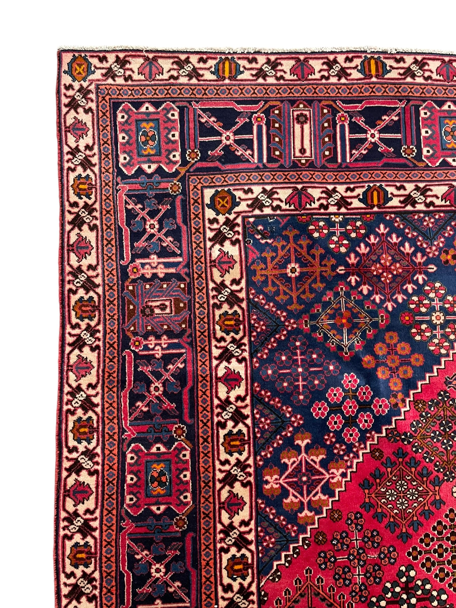 Persian Joshaghan red ground rug, the medallion, field and spandrels decorated with Pitrak and tree of life motifs, the border with repeating design decorated with stylised plant motifs, within guard stripes