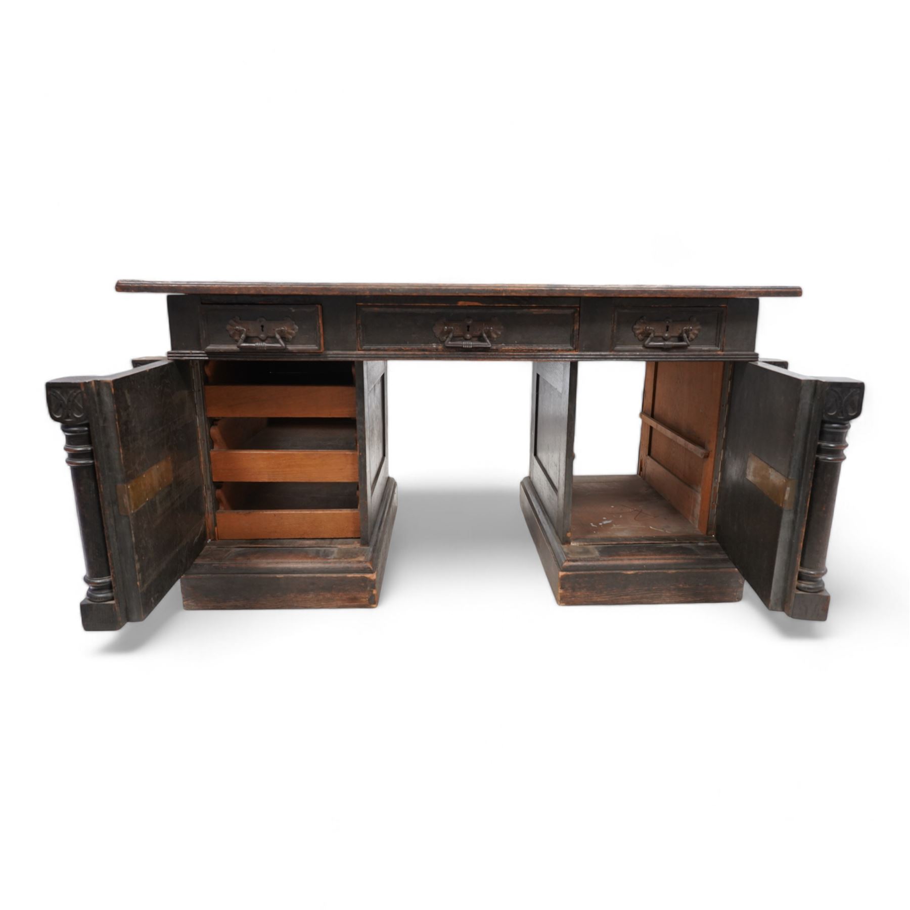 Late Victorian oak twin pedestal desk, rectangular moulded top with brown leather inset, three drawers fitted with Aesthetic Movement angular handles, each pedestal enclosed by door with turned columns, on moulded plinth base 