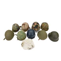 Collection of nine military helmets, including several with camouflage covering 