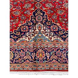 Persian Kashan crimson ground rug, overall arabesque design, the field decorated with swirled leafy branches and palmettes, indigo ground border decorated with repeating pattern, within guard stripes 