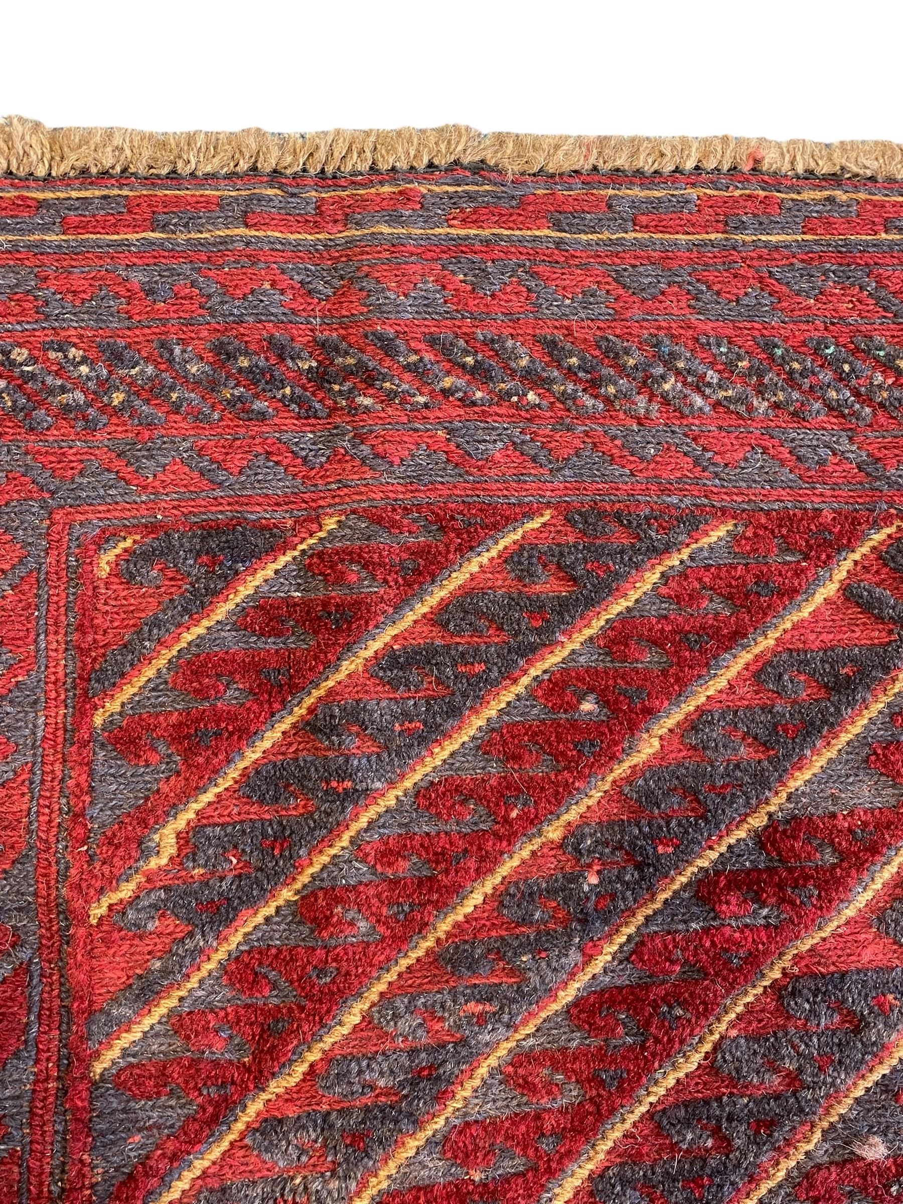 Meshwani indigo and maroon ground rug, the field decorated with a central lozenge with concentric borders containing hook motifs, enclosed by geometric zig-zag guard lines