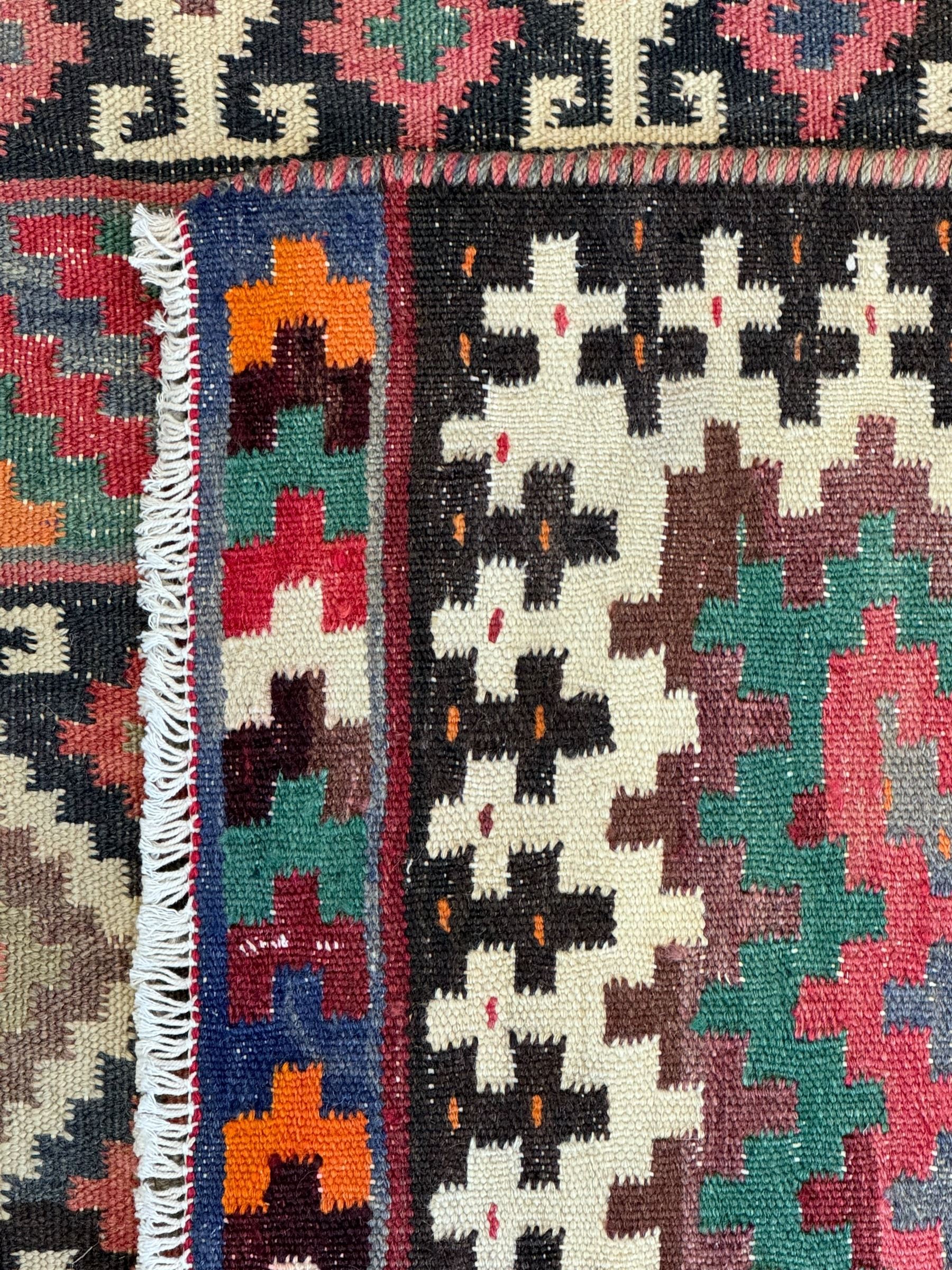 Northeast Persian Sumak Kilim red ground rug, the field decorated with rows of multicoloured diamond motifs featuring  geometric patterns, the border composed of alternating black and white stepped designs, enclosed by a narrow band with multicoloured geometric shapes