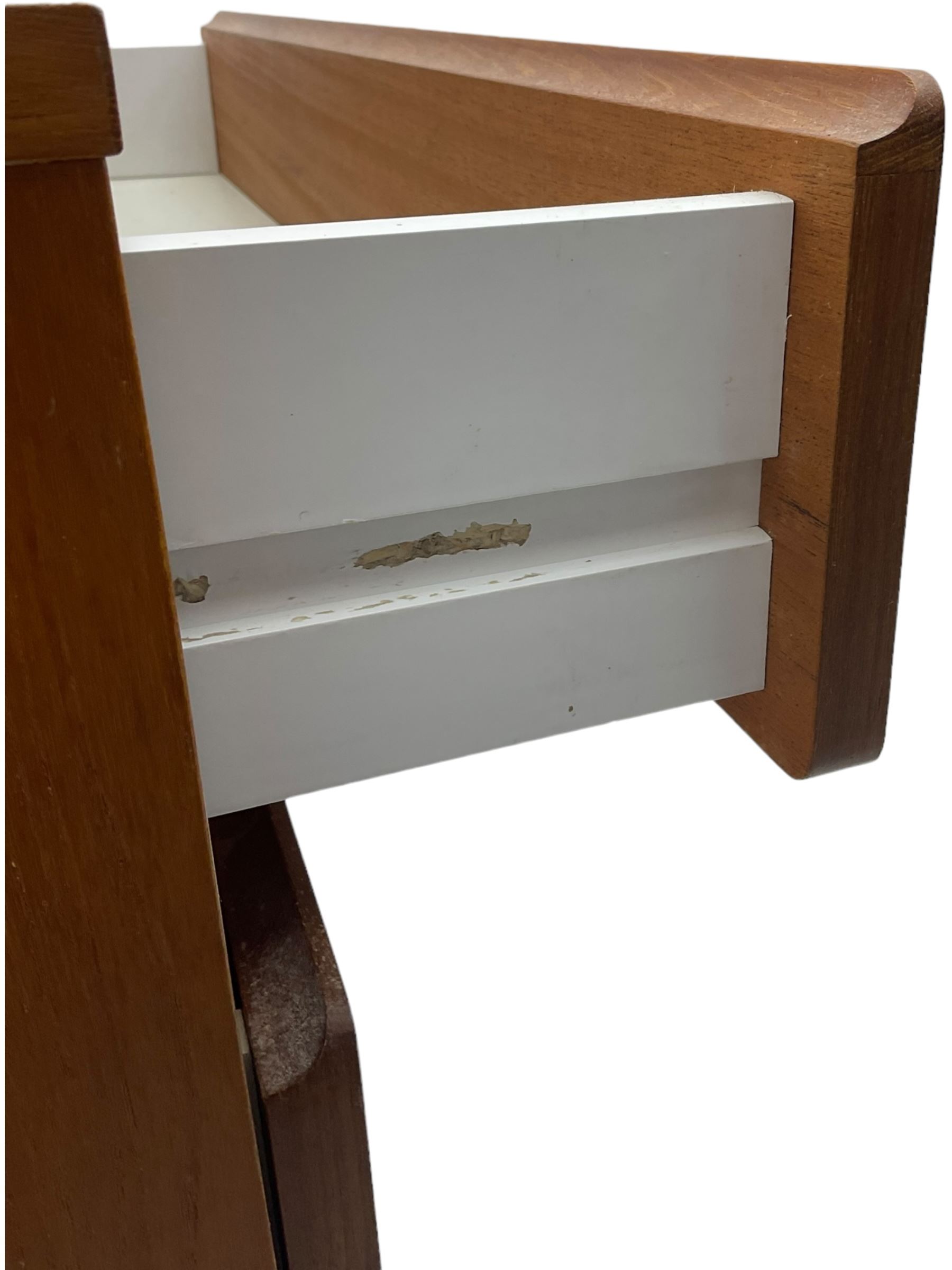 Mid-20th century teak four-drawer chest, featuring a minimalist design with two shallow and two deep flush drawer fronts, each with recessed handles along the top edge, the drawers open to reveal white laminate interiors, supported by castors