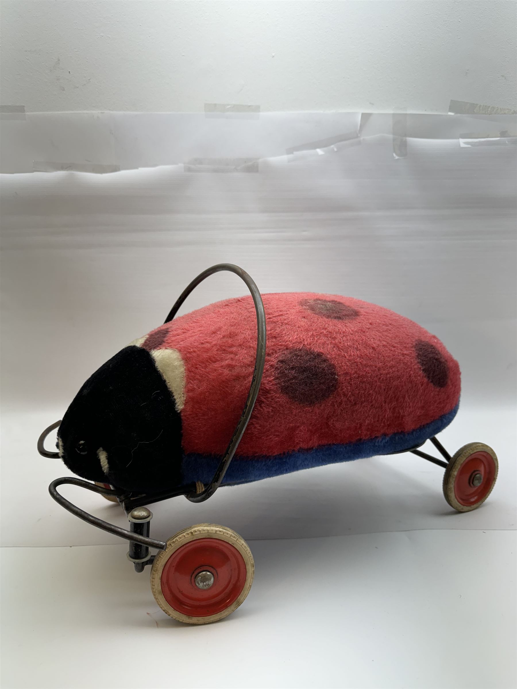 Steiff child's ride on ladybird, circa 1950s, the mohair body with red and black spotted seat, black and white face and blue underbelly, upon a metal frame with rubber and metal wheels, H30cm, W52cm