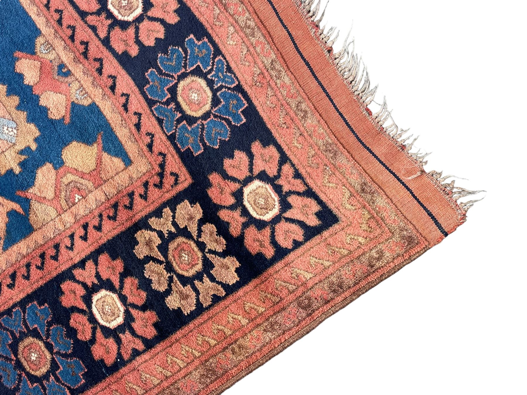 Afghan rust ground carpet, large central lozenge medallion decorated with stylised plant motifs, running water guard stripes enclosing indigo ground border decorated with stylised flower heads