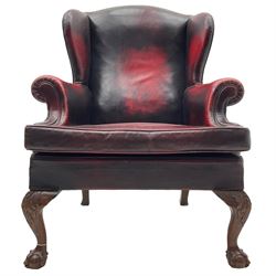 Georgian design hardwood-framed wingback armchair, upholstered in red leather, loose seat cushion and rolled arms, on acanthus carved ball and claw front feet 