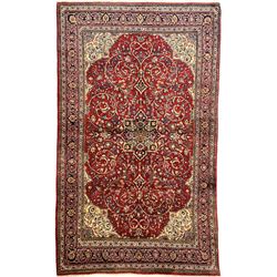 North west Persian Sarouk crimson ground rug, central floral medallion surrounded by scrolling branches decorated with foliage and stylised plant motifs, the main border decorated with repeating scrolling design with floral motifs, within guard stripes 