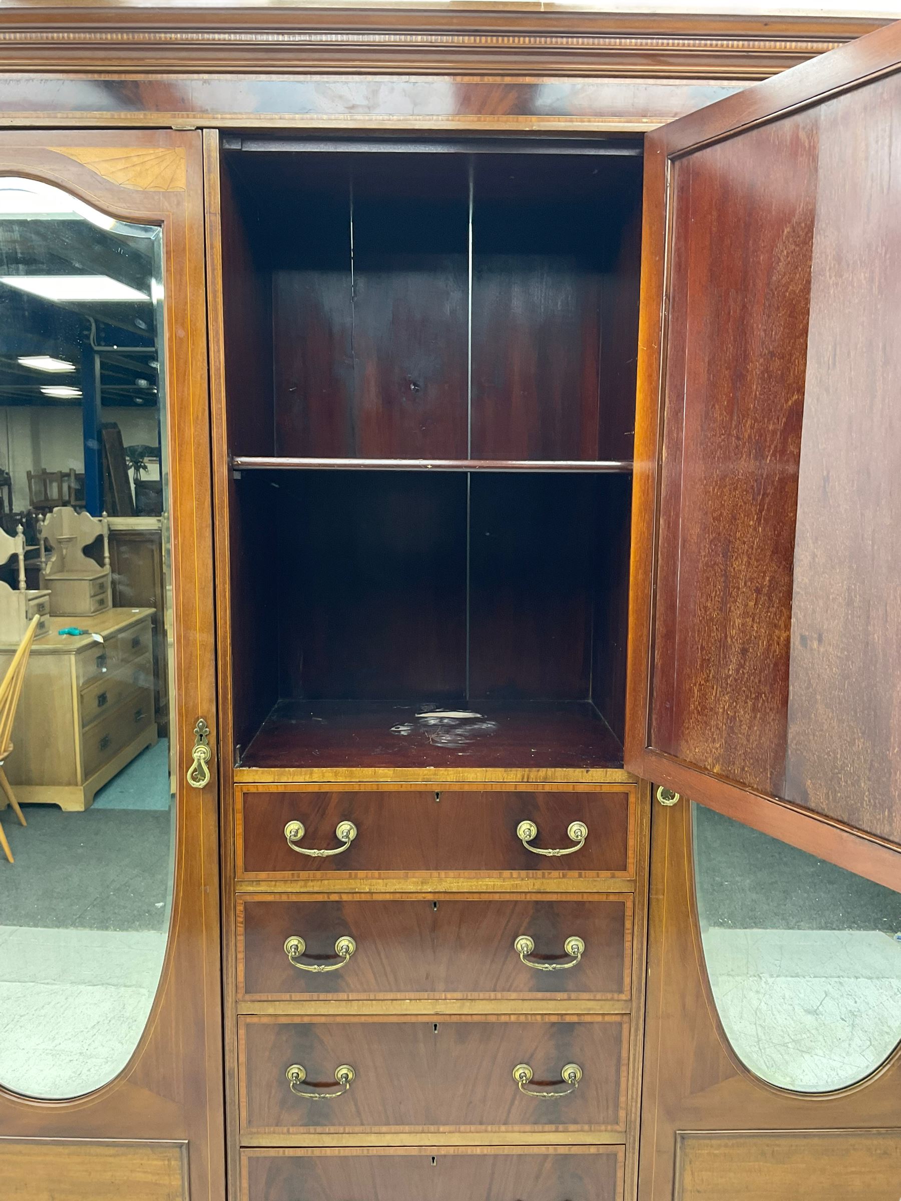 Edwardian inlaid mahogany combination wardrobe, projecting moulded cornice over figured frieze with satinwood banding, the central section fitted with cupboard over four long drawers, figured matched veneers and satinwood bands, flanked by two full height compartments enclosed by bevelled shield shaped mirror doors, satinwood fan inlaid spandrels, on moulded skirt base 