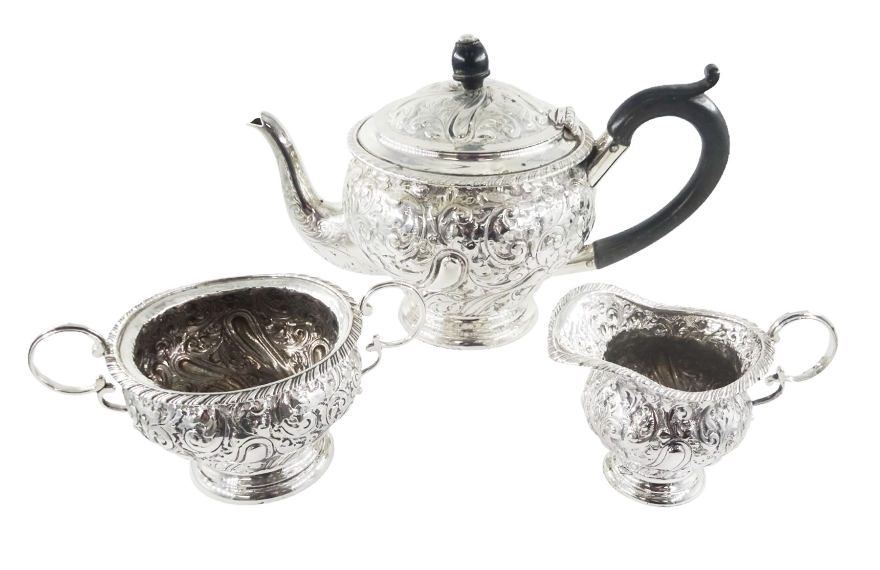 Late Victorian silver three piece bachelors tea service, comprising teapot, open sucrier and milk jug, each of bellied form, upon a circular stepped foot, and profusely embossed with foliate and scrolling decoration, the teapot with ebonised handle and finial, hallmarked George Nathan & Ridley Hayes, Birmingham 1894, teapot H14.5cm