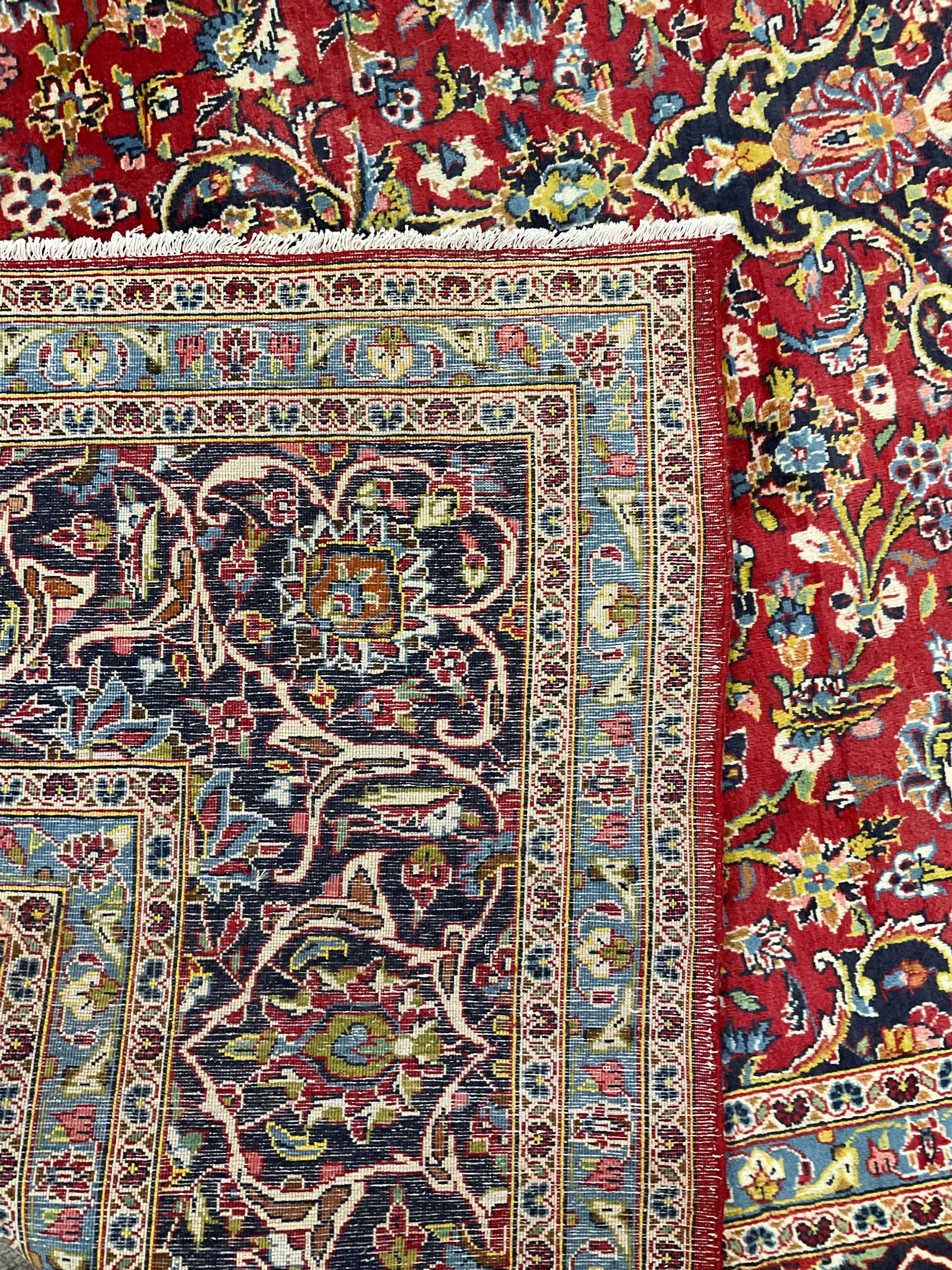 Persian Kashan crimson ground carpet, floral design central medallion surrounded by trailing leafy branches and stylised plant motifs, multi-band border with repeating floral design