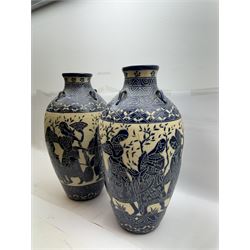 Pair of blue and white Cretan style vases, decorated with figures among trees with blue boarders on a white ground, H55cm