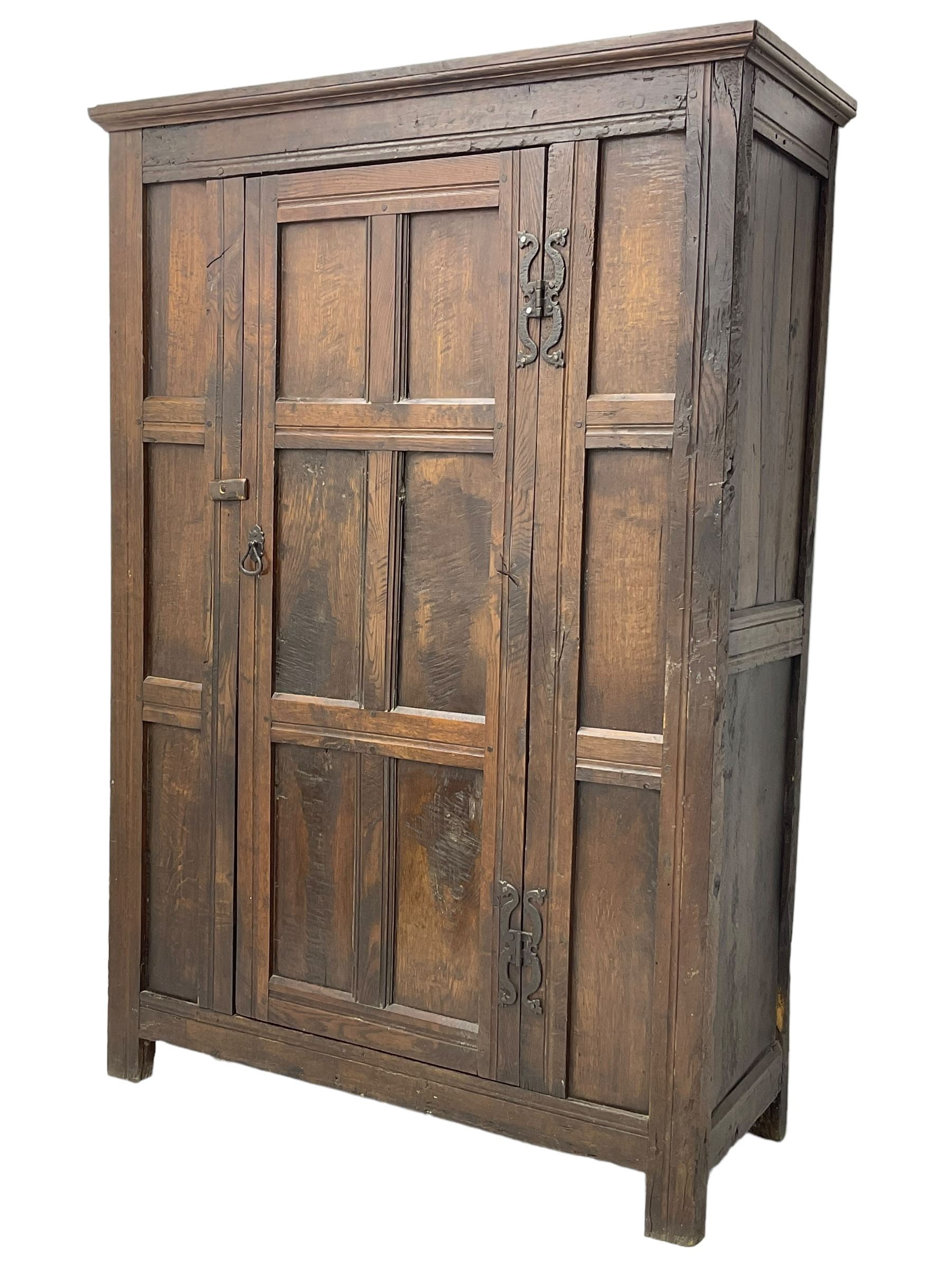 17th century and later oak hall cupboard, panelled front and sides with moulded frame, enclosed by single door with wrought metal hinges and handle, the interior fitted with hooks, on stile supports 