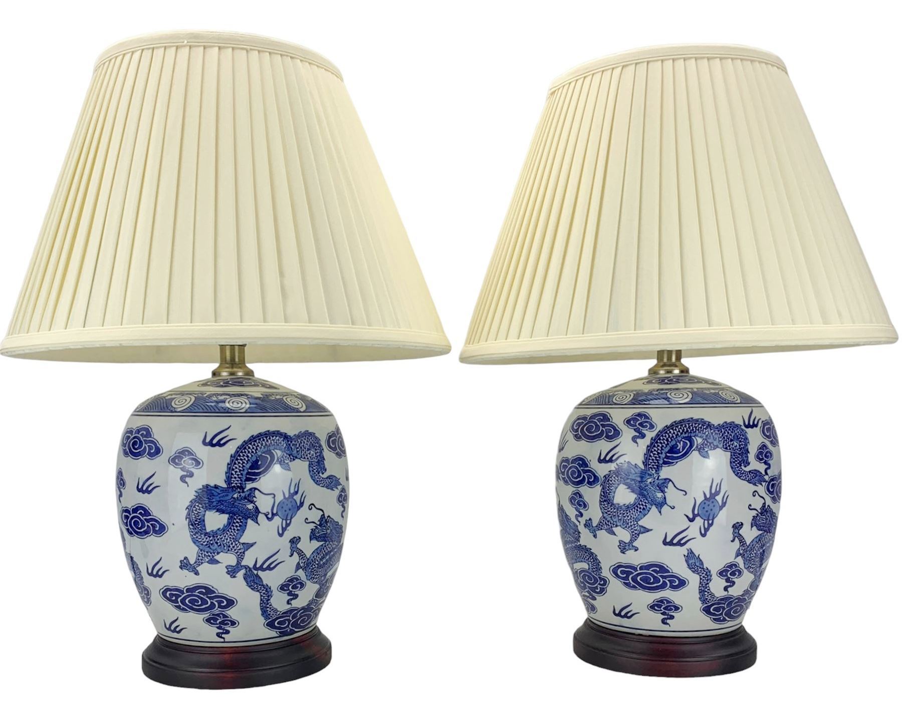 Pair of blue and white ovoid form table lamps, each decorated with dragons chasing the flaming pearl amidst clouds, raised upon circular hardwood bases, H28cm excluding fitting